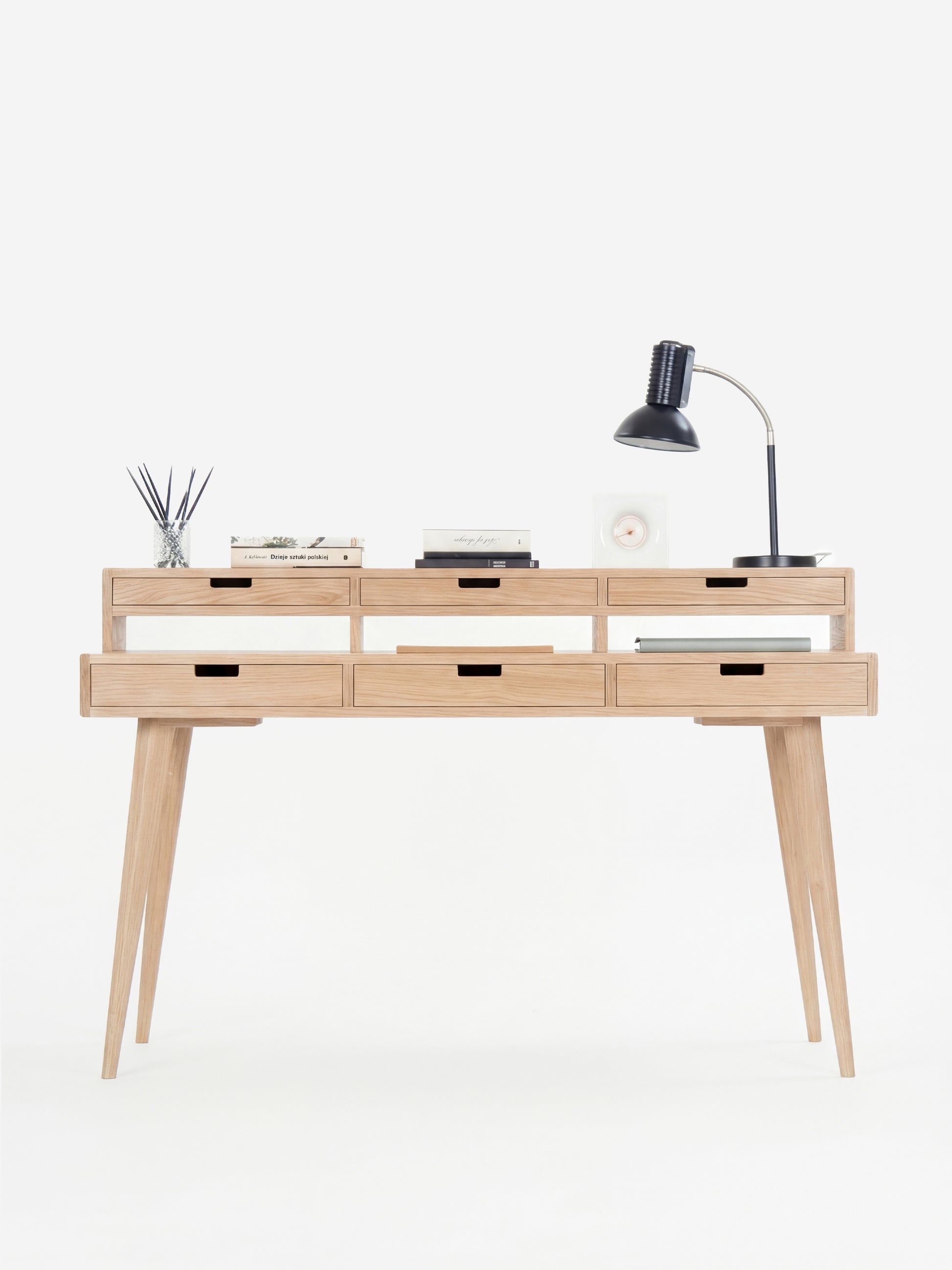 Minimalist wooden desk with six drawers, a table lamp, books, and a diffuser.