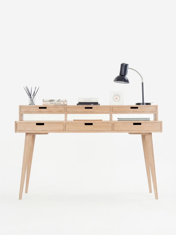Minimalist wooden desk with six drawers, a table lamp, books, and a diffuser.
