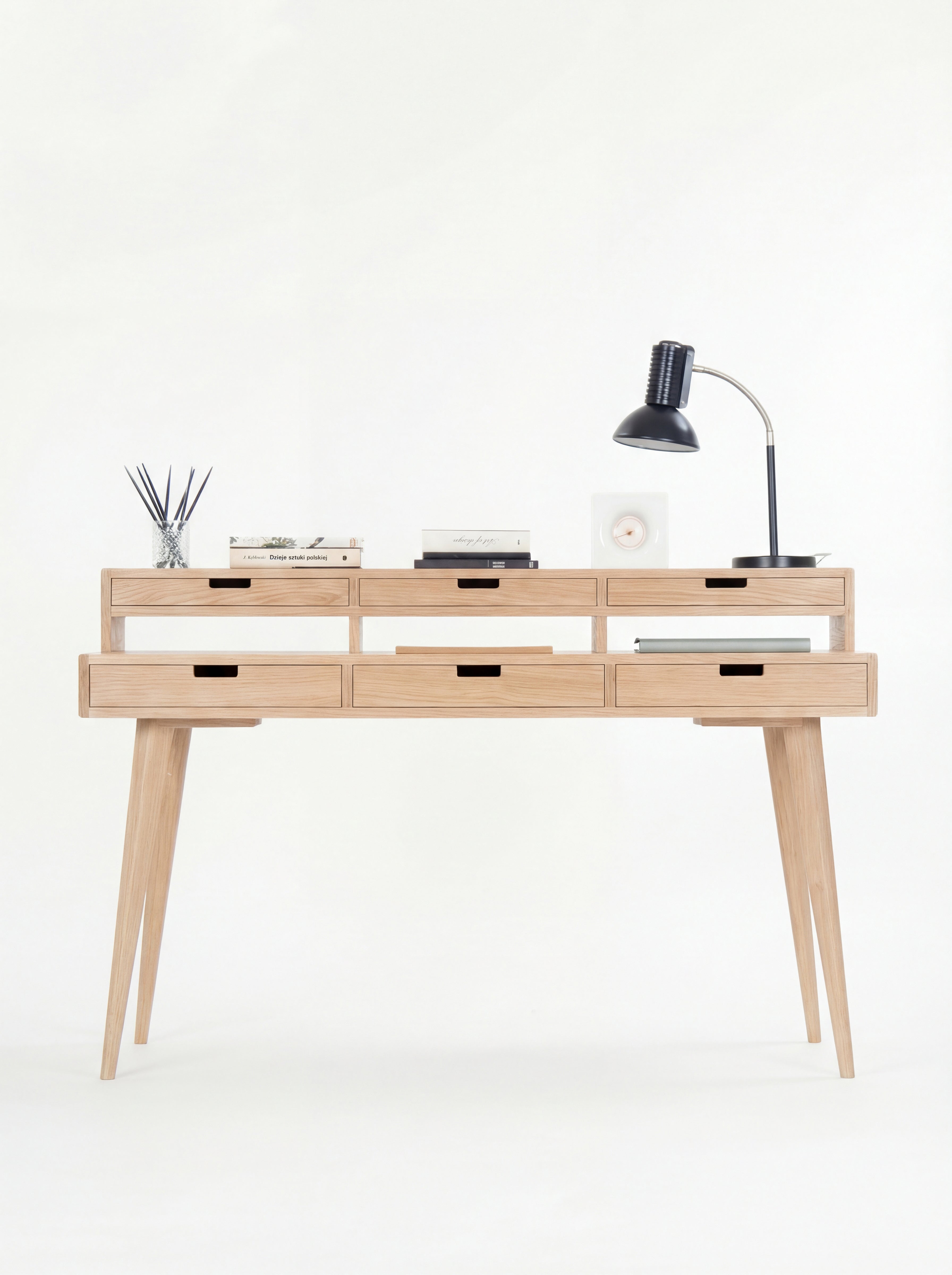 Minimalist wooden desk with six drawers, a table lamp, books, and a diffuser.