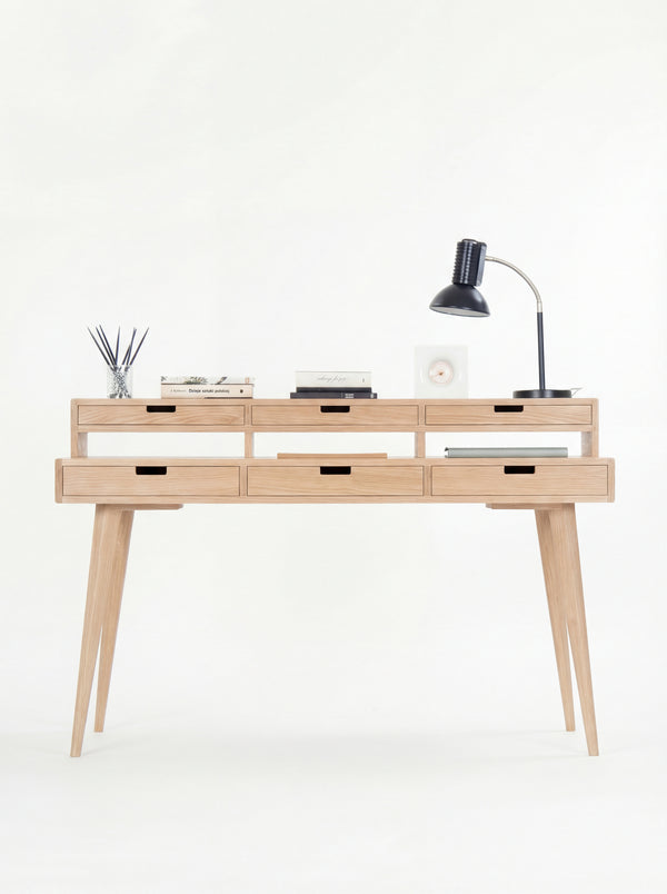 Minimalist wooden desk with six drawers, a table lamp, books, and a diffuser.