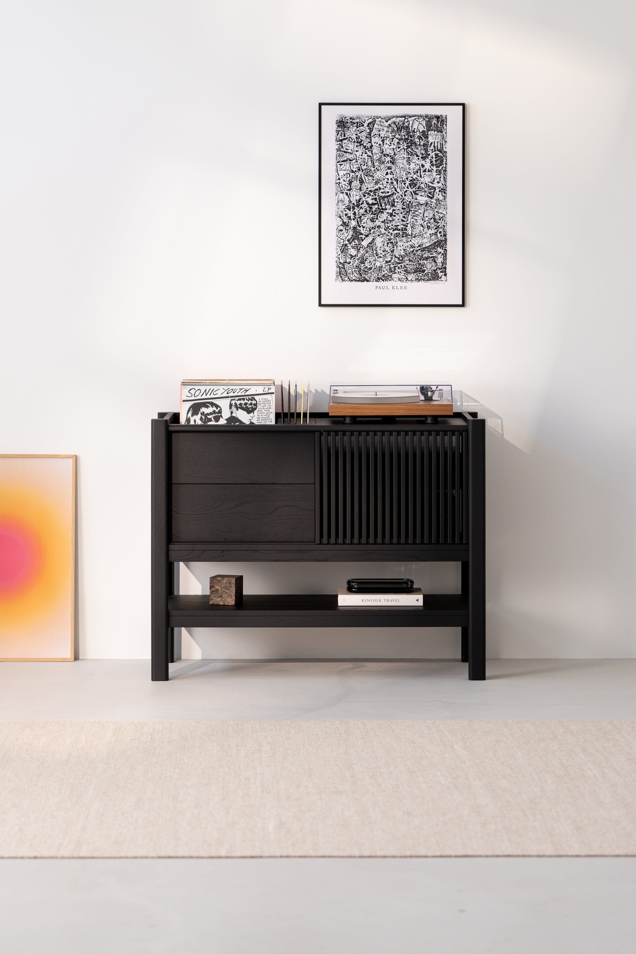 Black cabinet with vinyl records and a turntable, framed art above, and gradient artwork on the floor.