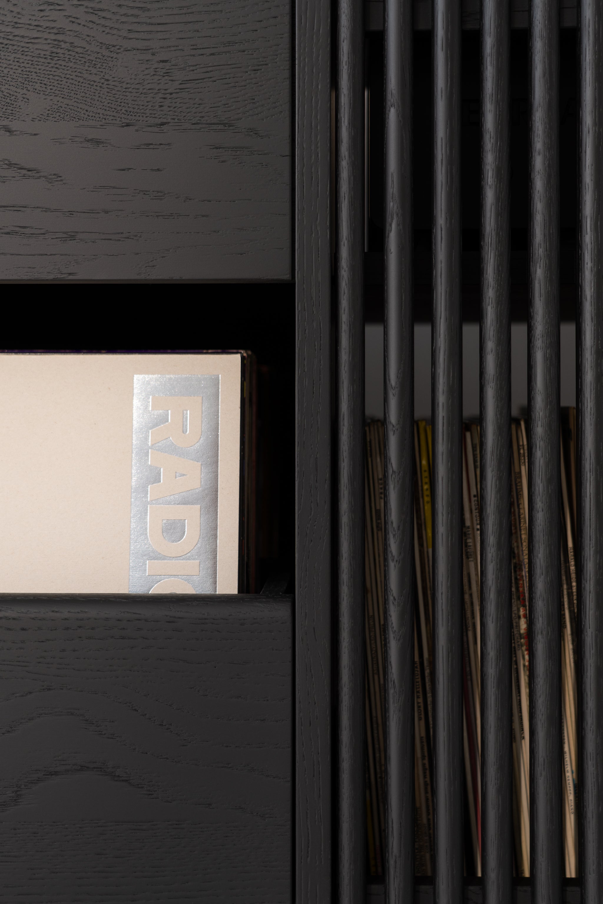 Close-up of a black shelf with a beige book and vertical slats revealing more books behind.