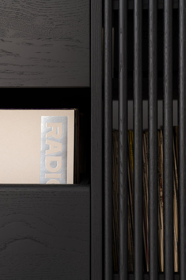 Close-up of a black shelf with a beige book and vertical slats revealing more books behind.