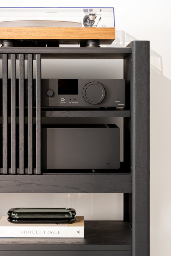Audio equipment on a dark shelf with books and a glass container below.