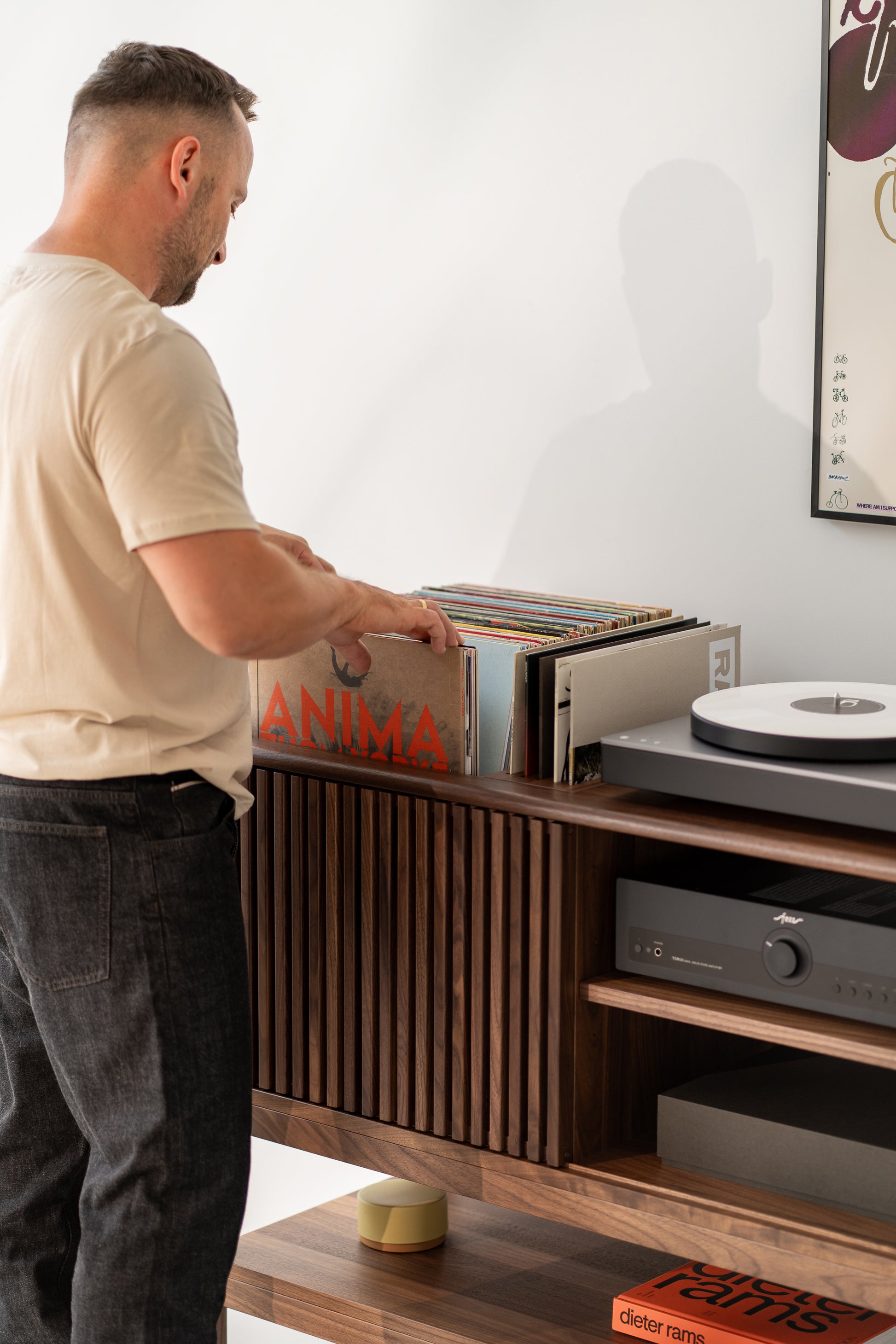  Man browsing vinyl records next to a turntable and stereo on a wooden shelf.