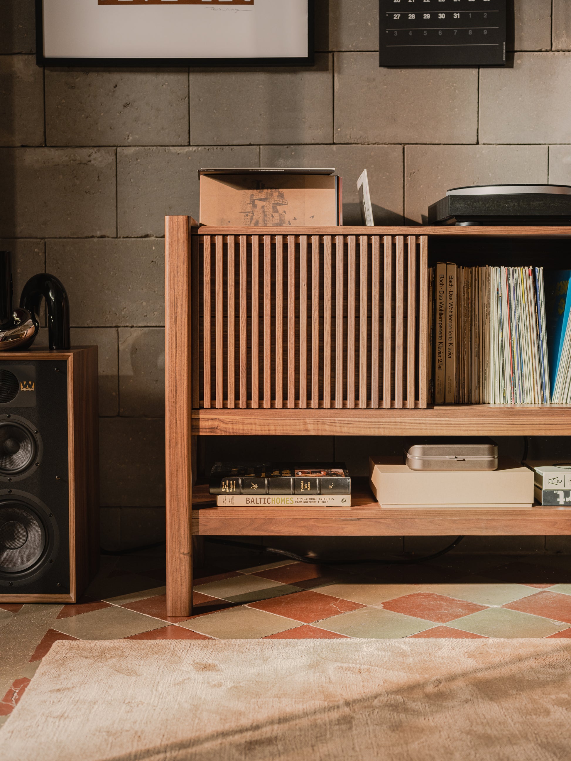 Wooden shelf with vinyl records, books, and a speaker in a cozy, brick-walled room.