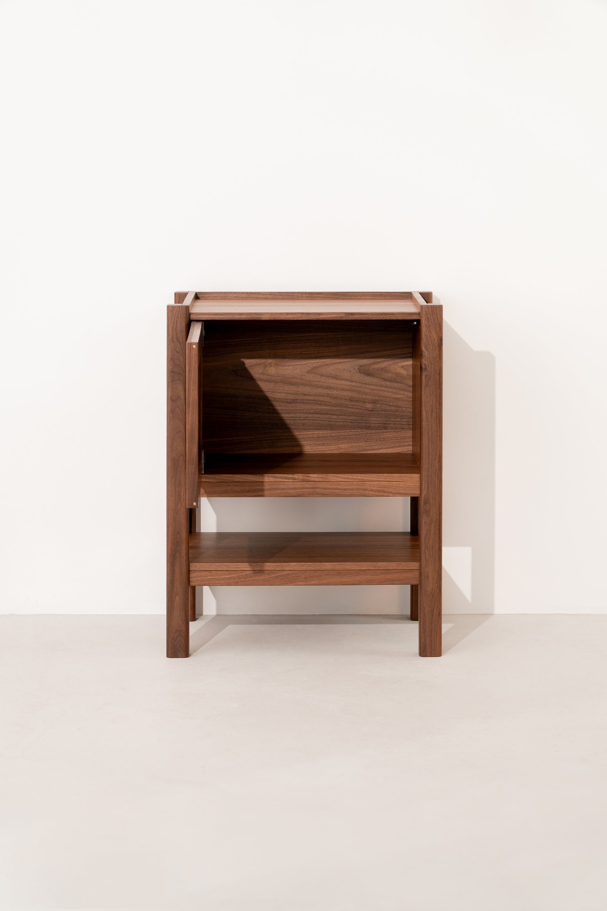 Wooden side table with a minimalist design, featuring an open shelf and a top compartment against a white wall.