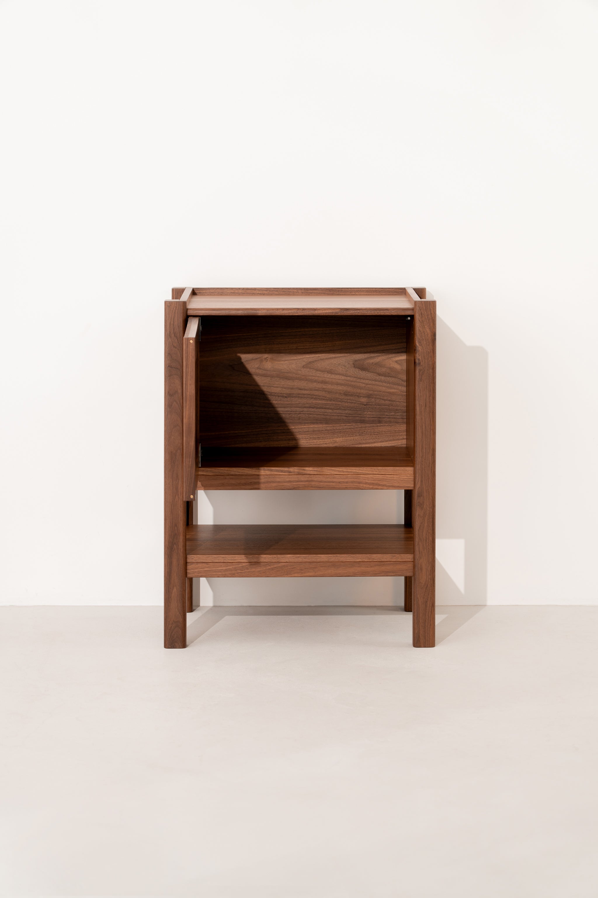 Wooden side table with a minimalist design, featuring an open shelf and a top compartment against a white wall.