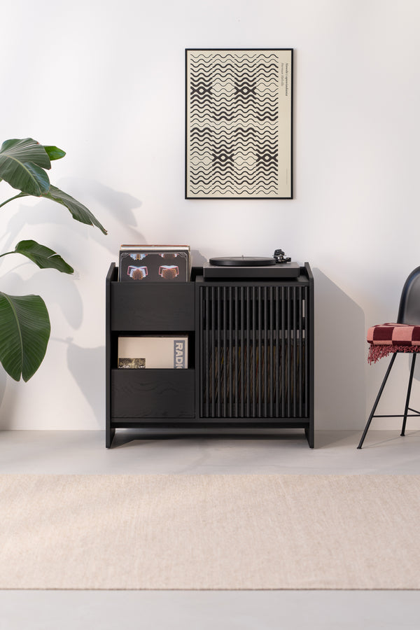 Minimalist room with a black record player stand, vinyl records, abstract wall art, and a chair.