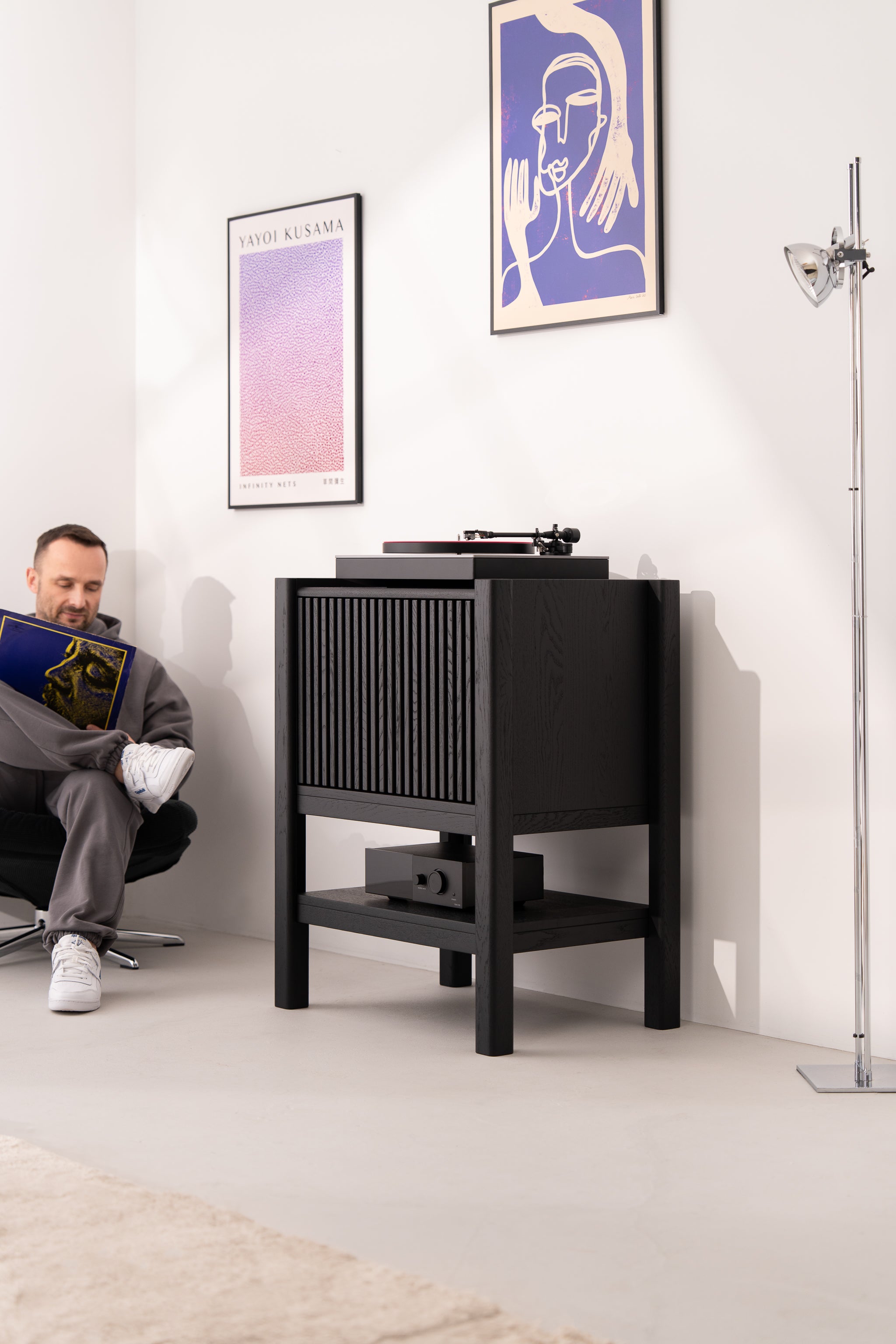 Man sitting and holding a record in a room with a turntable and art on the walls.