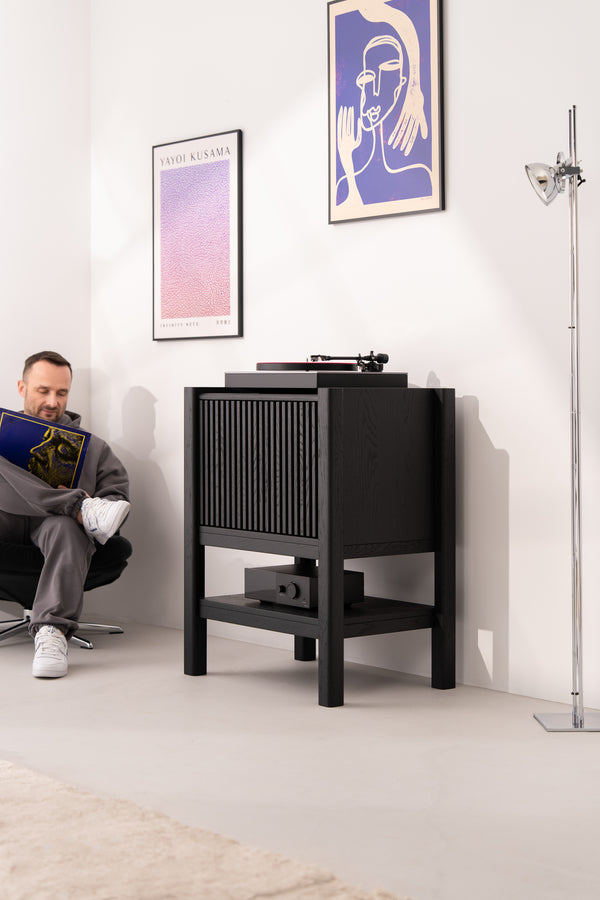 Man sitting and holding a record in a room with a turntable and art on the walls.
