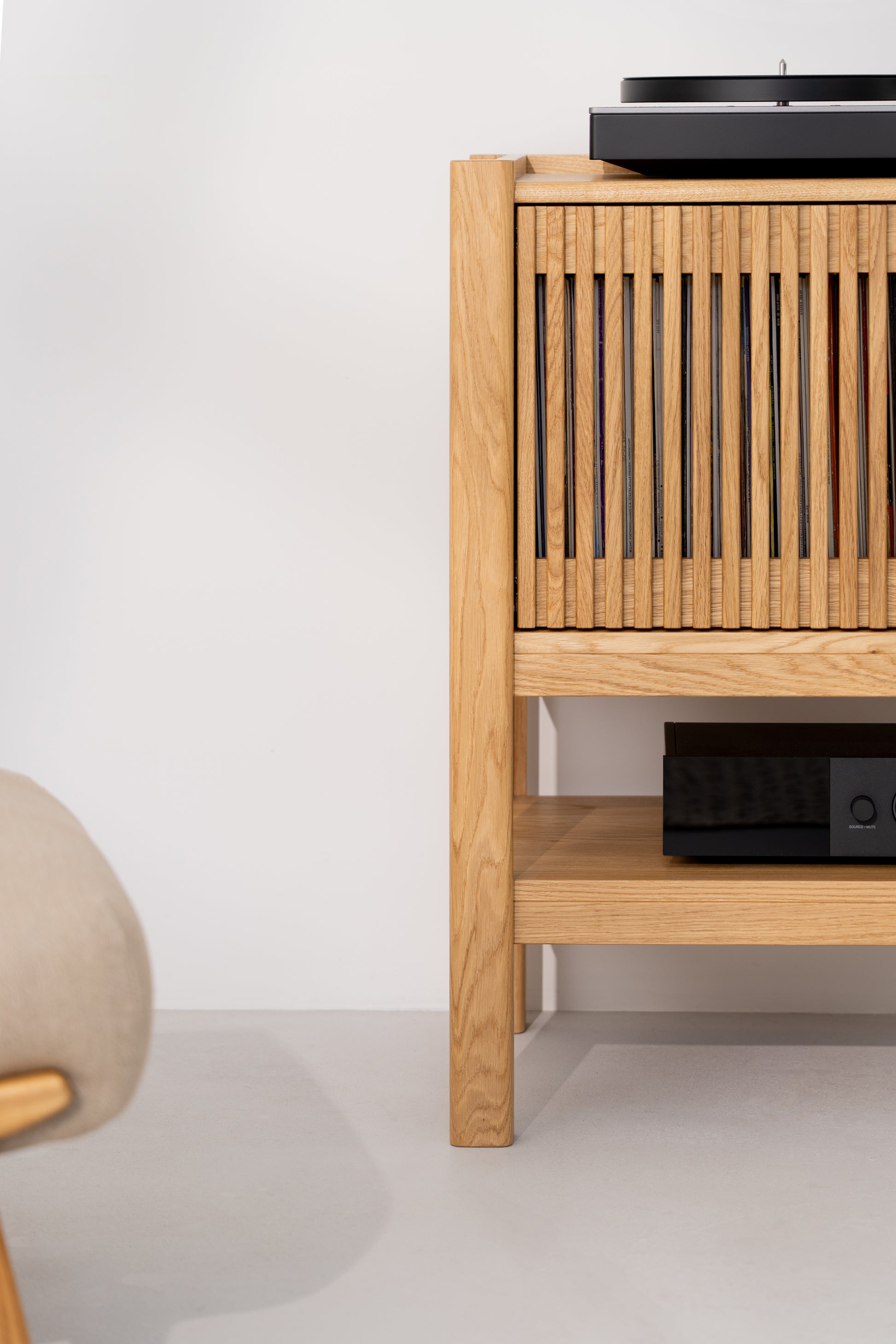 Wooden cabinet with slatted doors, turntable on top, and electronic device on a lower shelf.