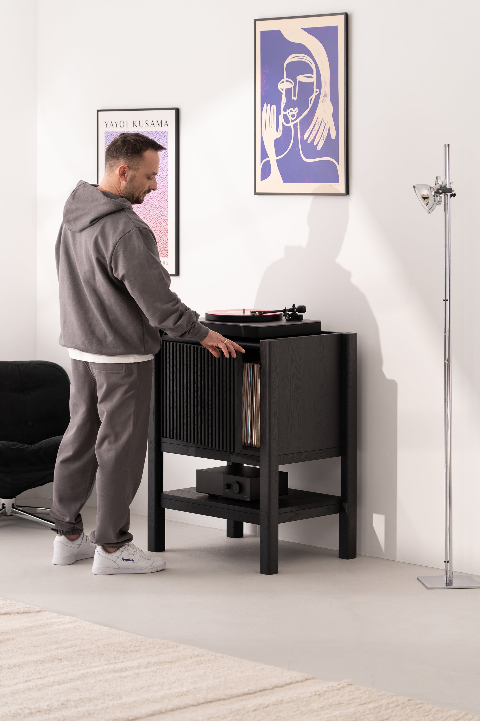 Person using a record player in a modern room with framed artwork on the wall.