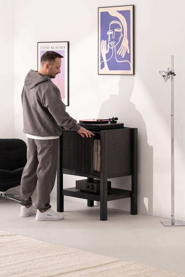 Person using a record player in a modern room with framed artwork on the wall.