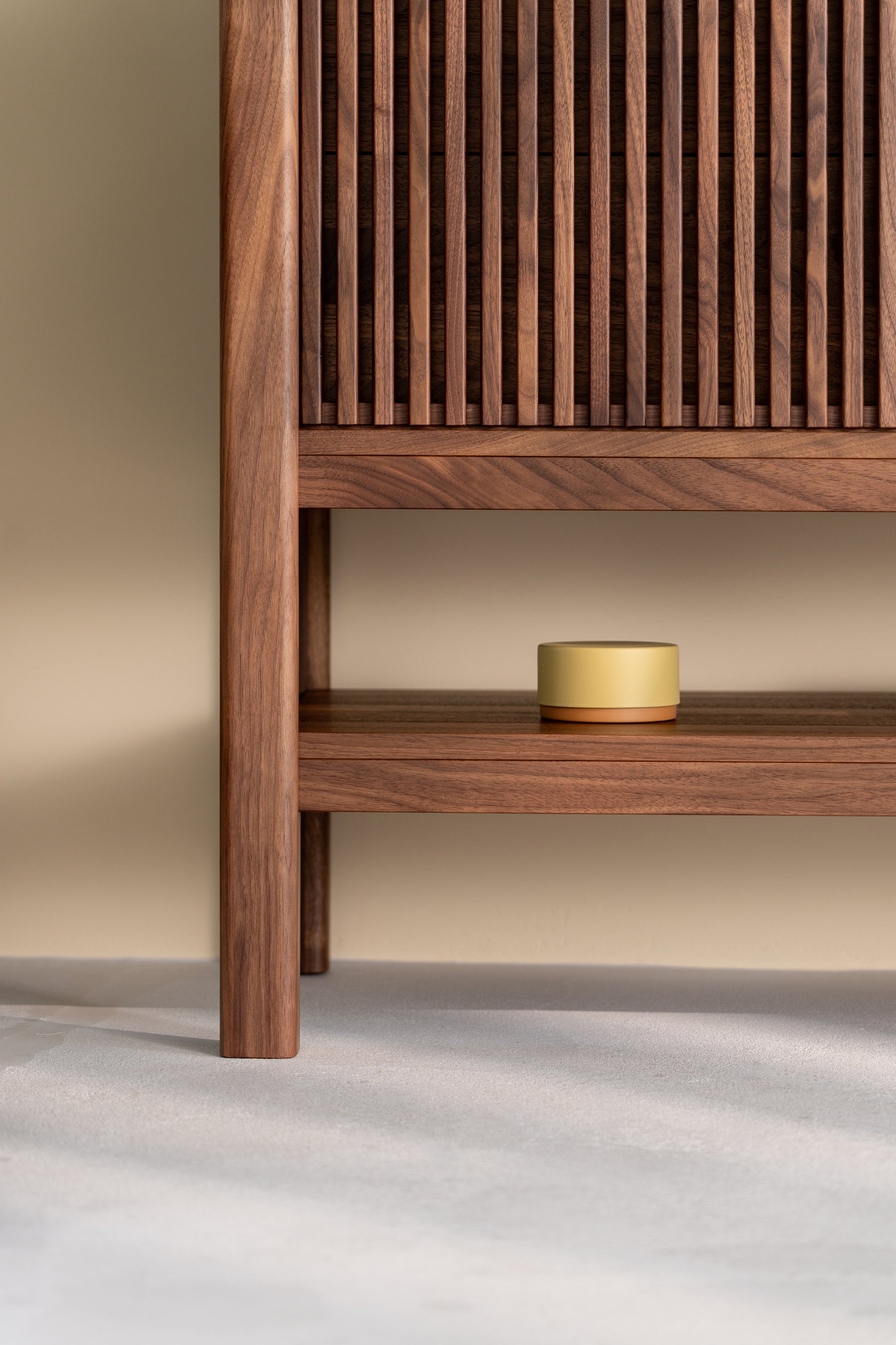 Wooden cabinet with slatted door, open shelf displaying a small round yellow container.