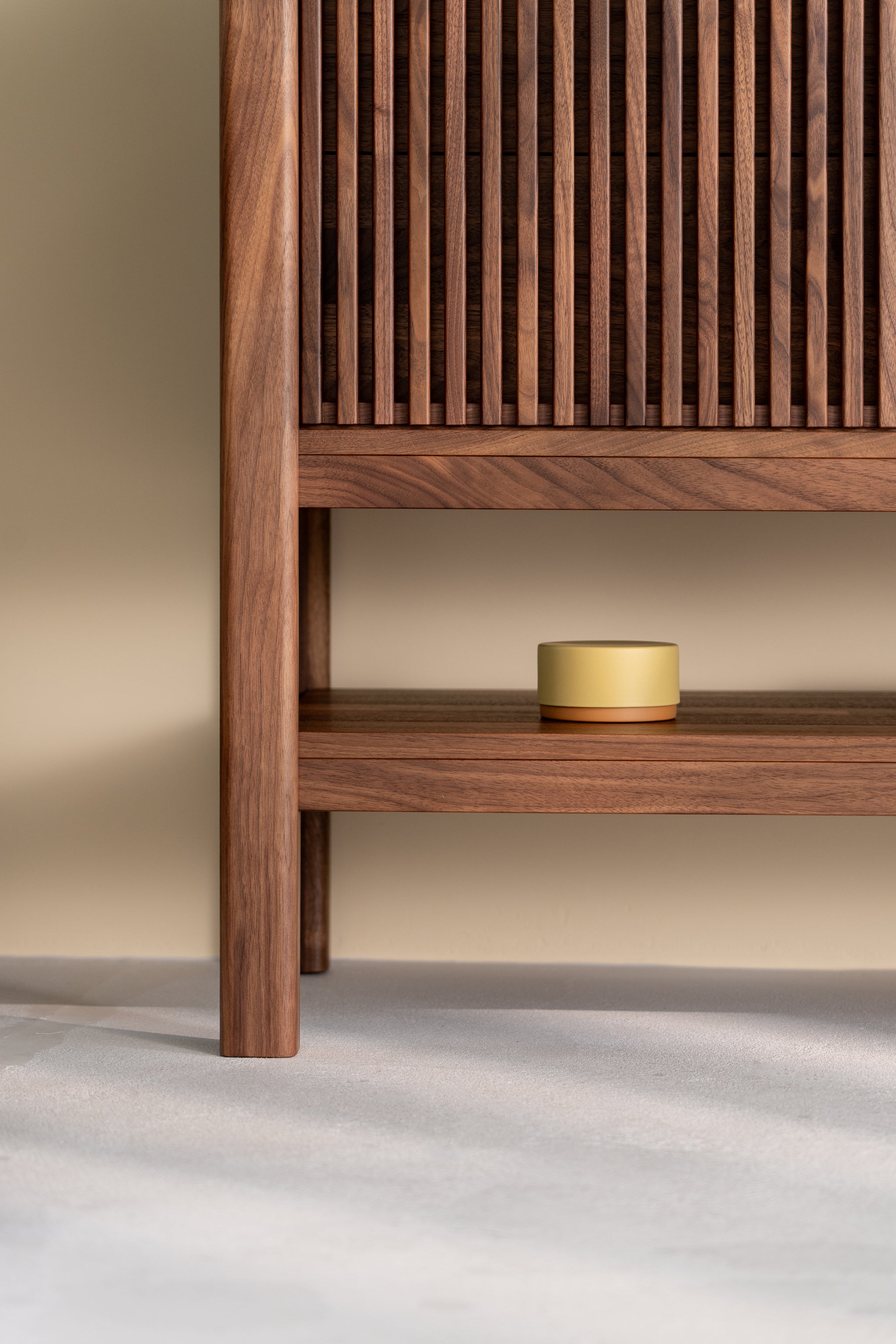 Wooden cabinet with slatted door, open shelf displaying a small round yellow container.
