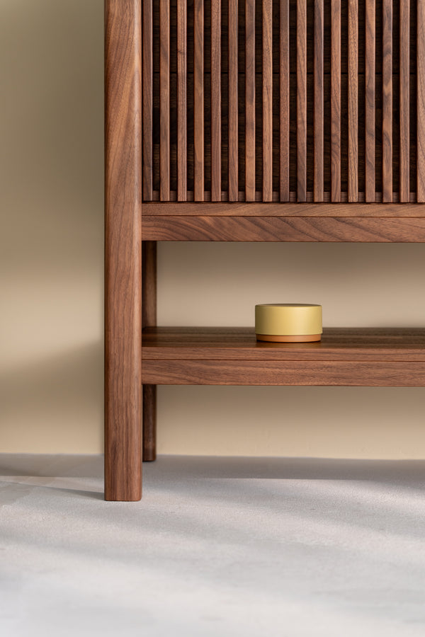 Wooden cabinet with slatted door, open shelf displaying a small round yellow container.
