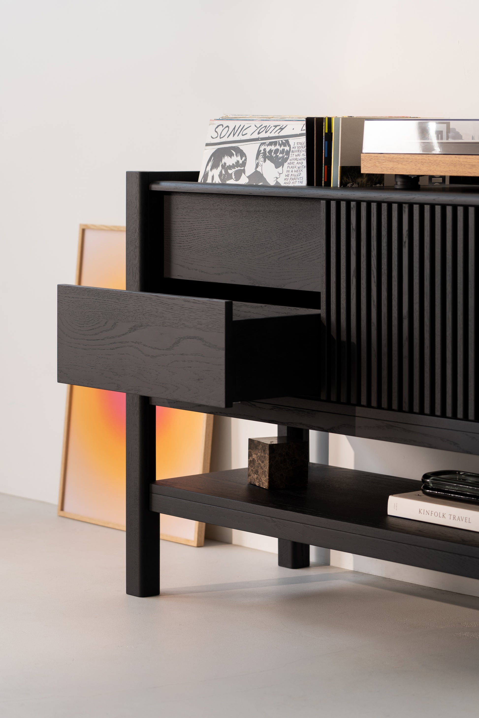 Black cabinet with open drawer, record albums, and a turntable. Sunset art and book with "KIN" visible below.