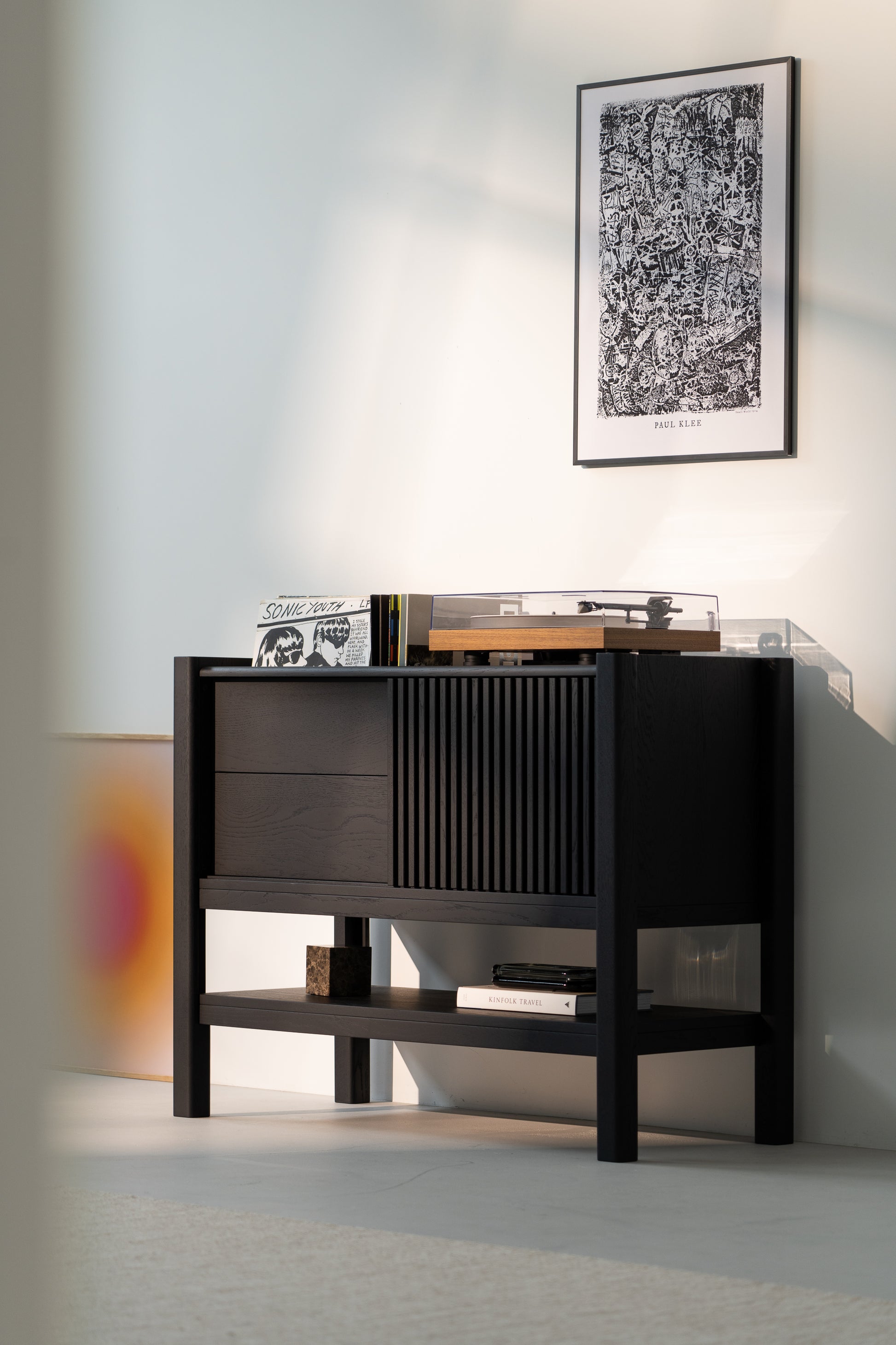 Dark wooden console with records and a turntable beneath art on a white wall.