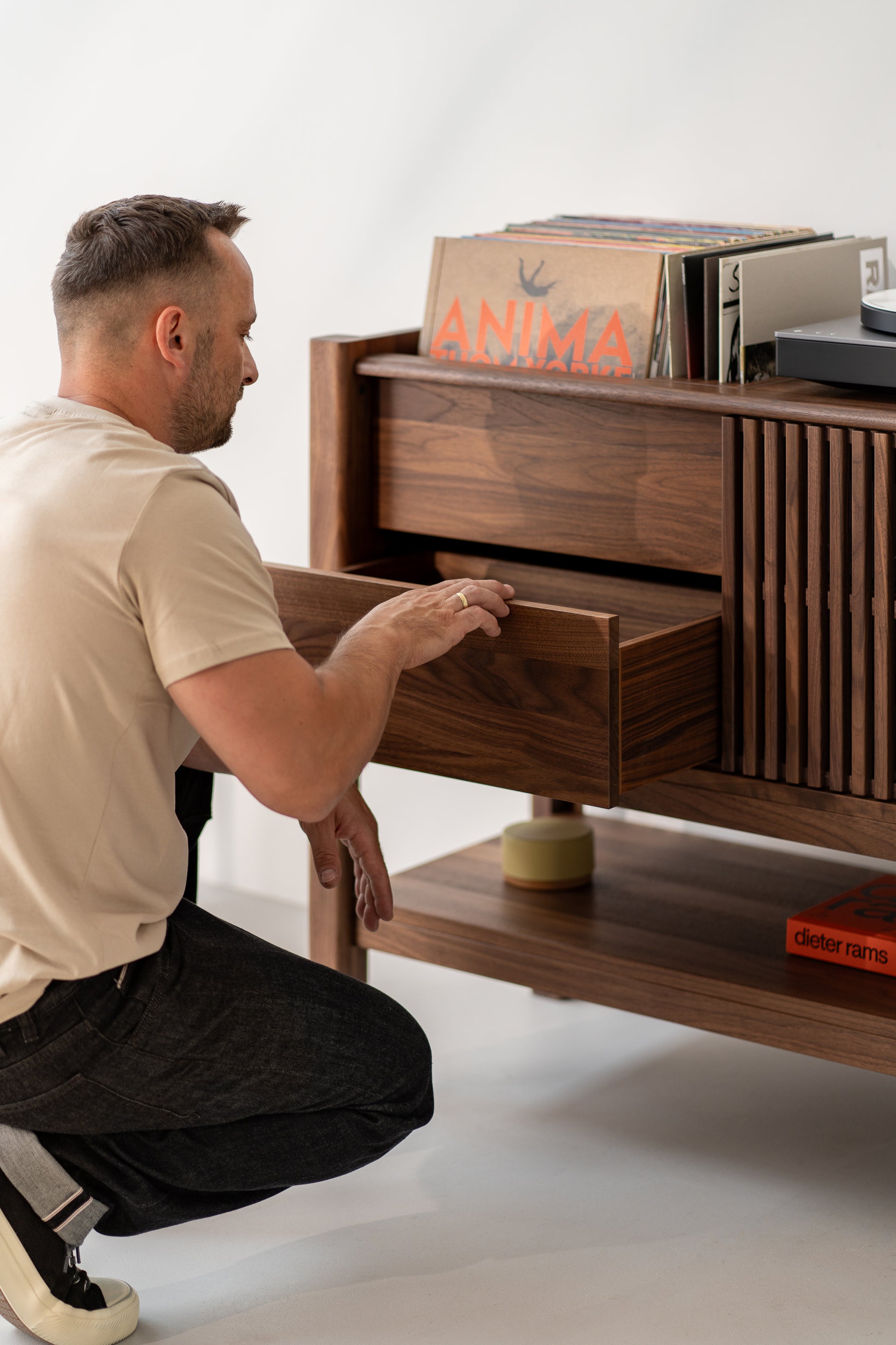 Man kneeling, opening a wooden drawer filled with vinyl records.