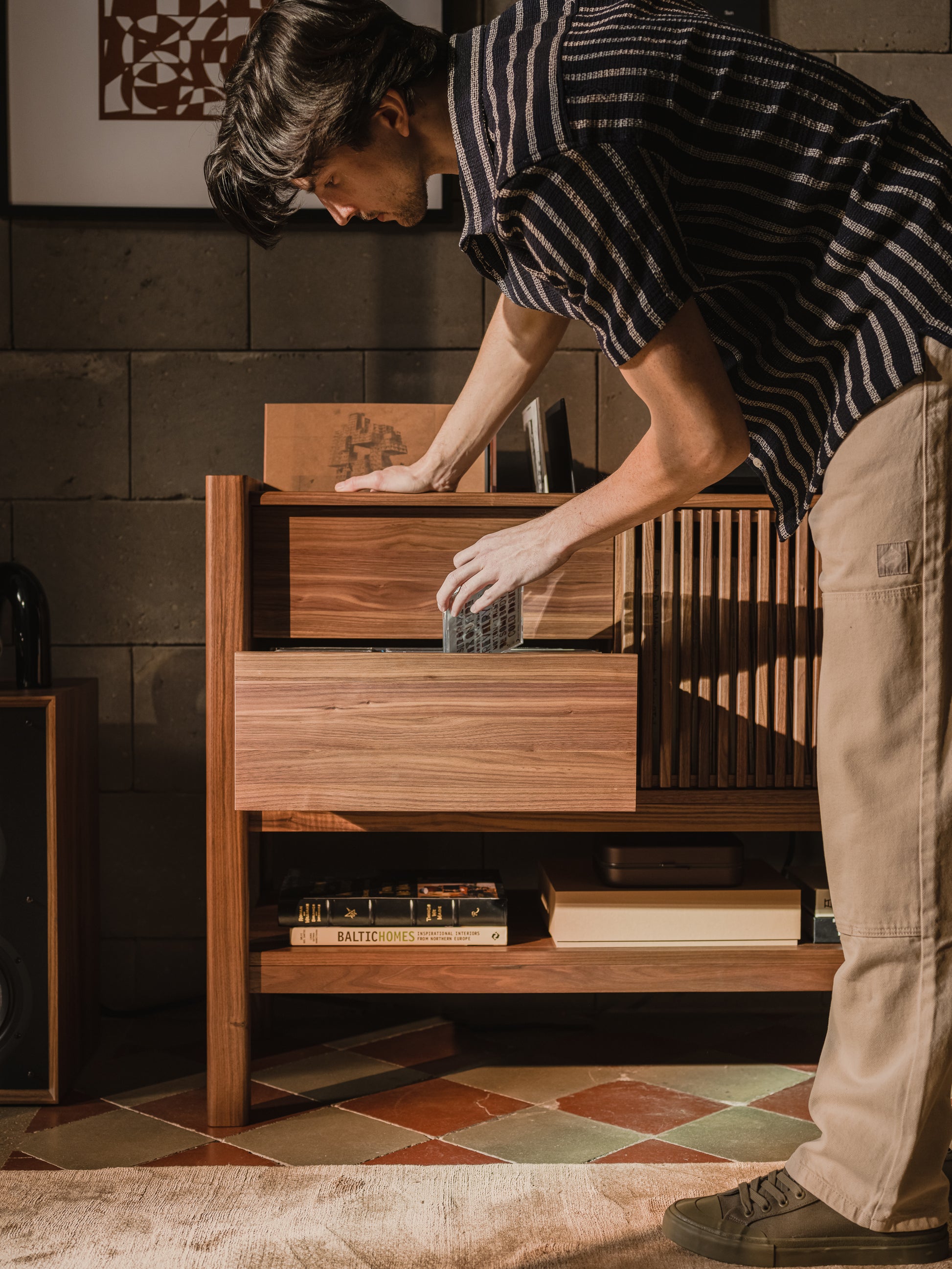 Person placing CD in a wooden cabinet, with books and artworks nearby.