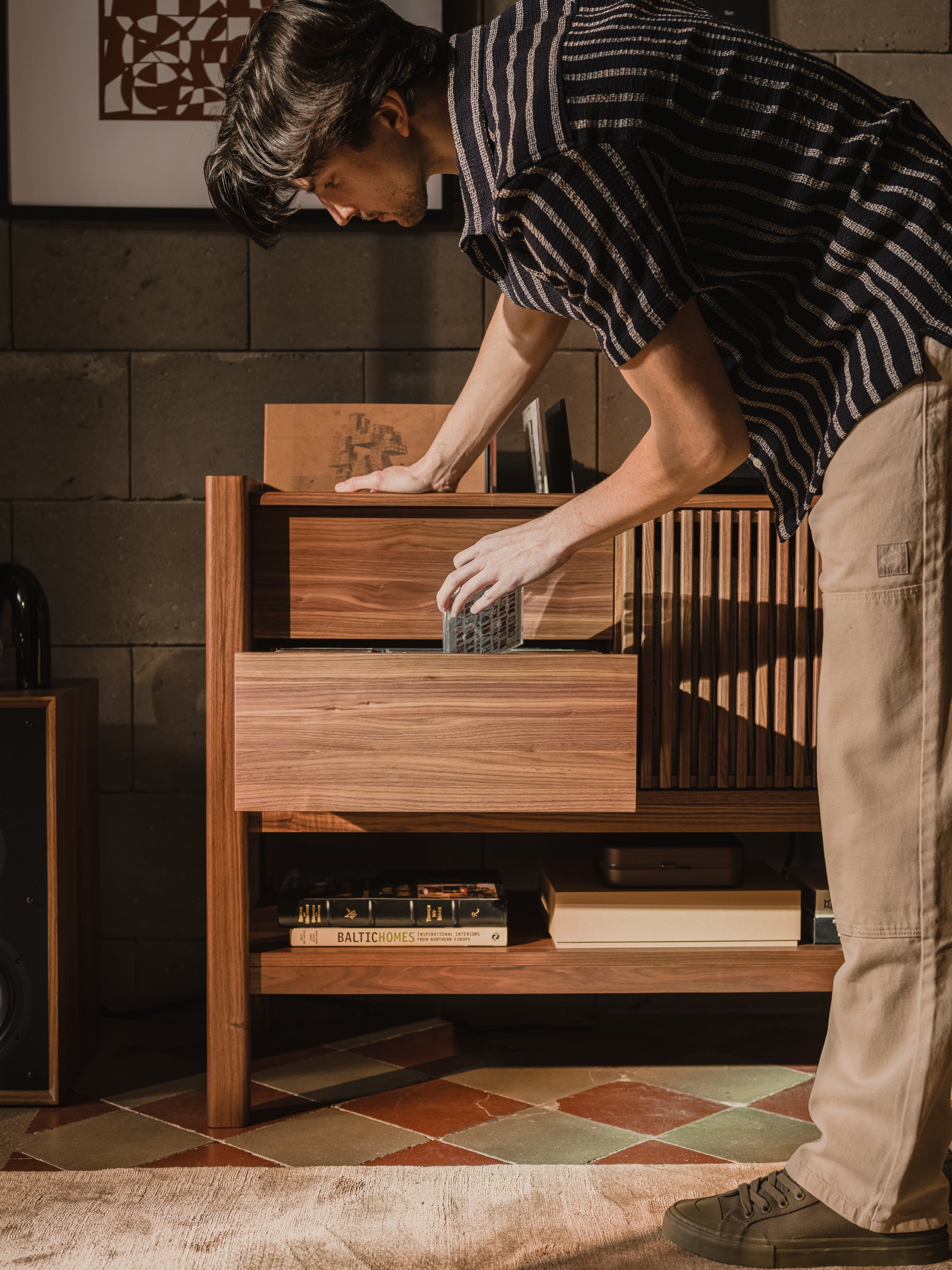 Person placing CD in a wooden cabinet, with books and artworks nearby.