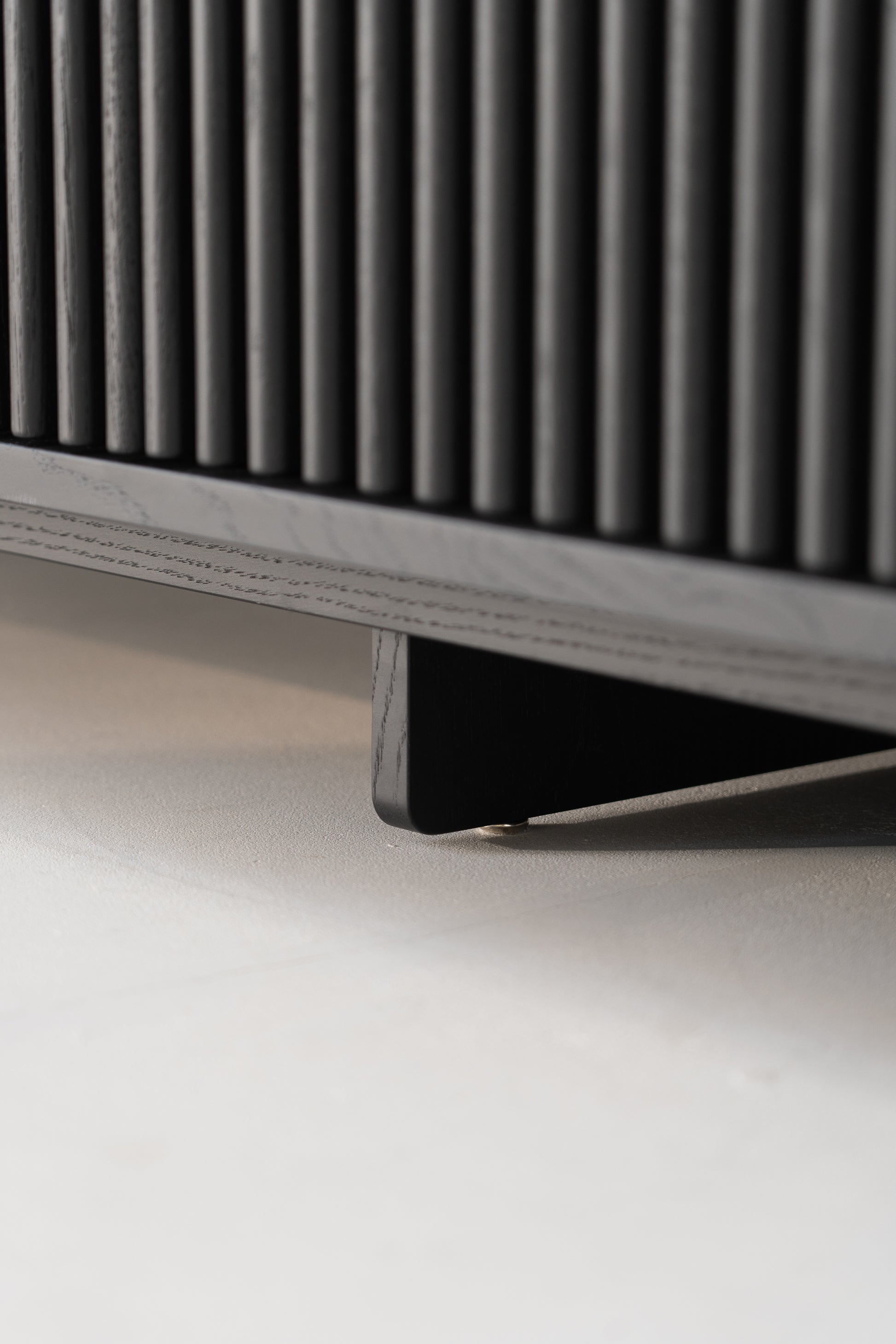 Close-up of the base of a black wooden cabinet with vertical grooves.
