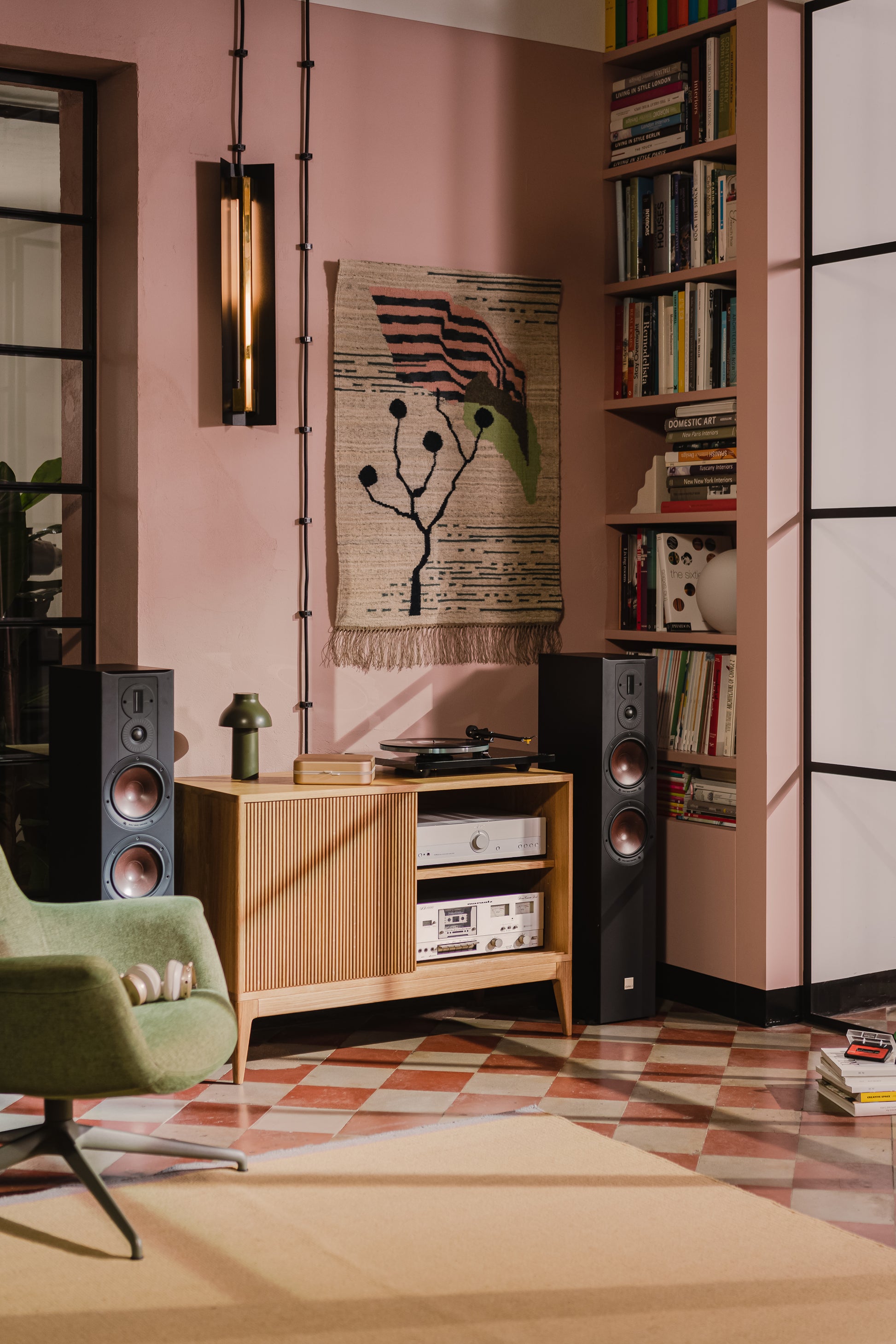 Cozy room with a record player, speakers, a green chair, and a woven wall hanging on a pink wall.