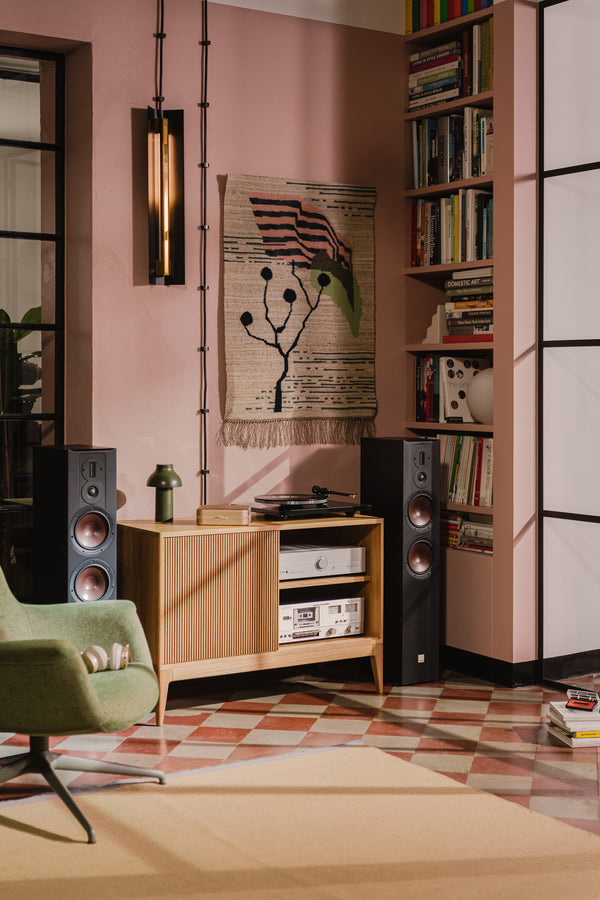 Cozy room with a record player, speakers, a green chair, and a woven wall hanging on a pink wall.