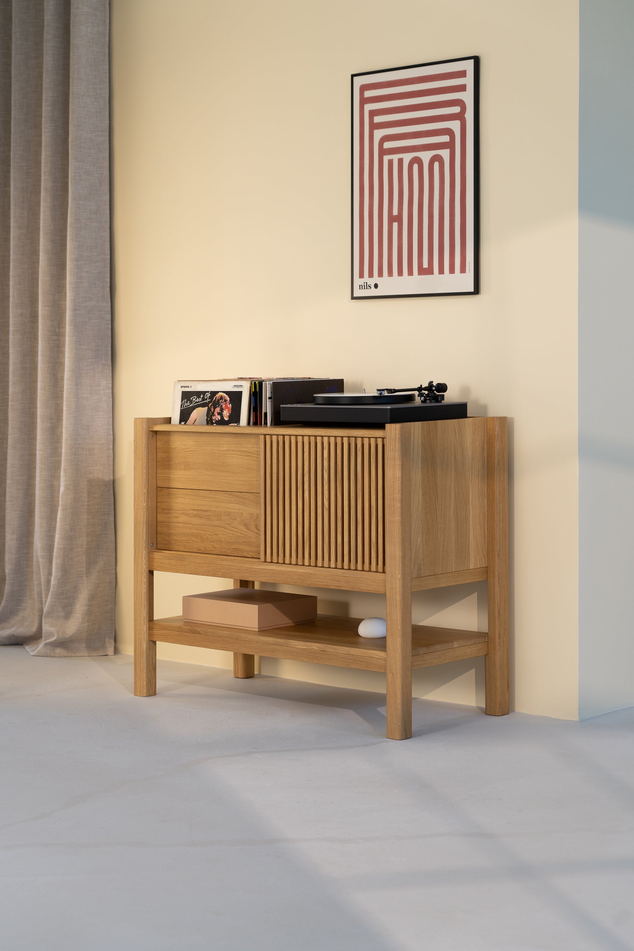 Wooden console with records and a turntable, beneath a geometric art print, next to beige curtains.
