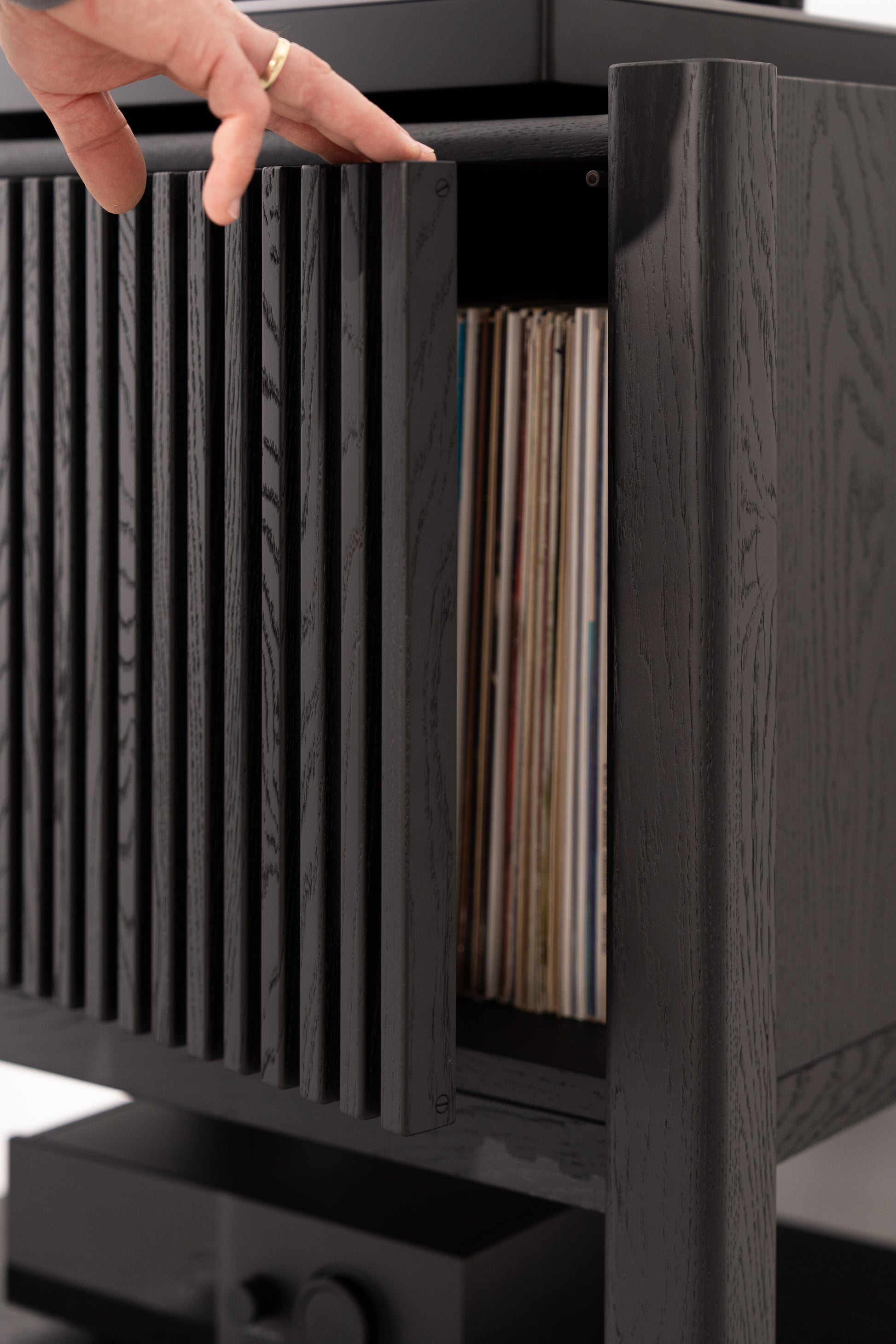 Hand opening black slatted cabinet revealing vinyl records inside.