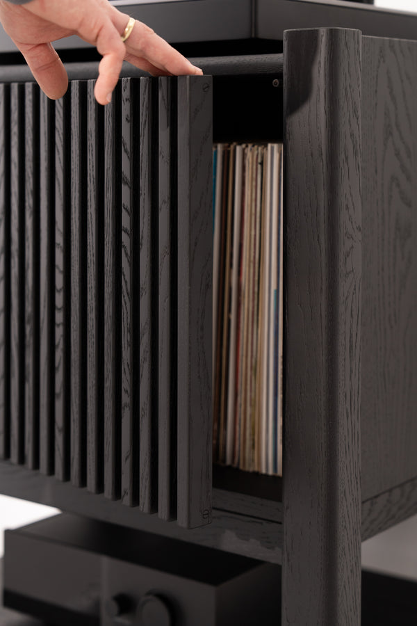 Hand opening black slatted cabinet revealing vinyl records inside.