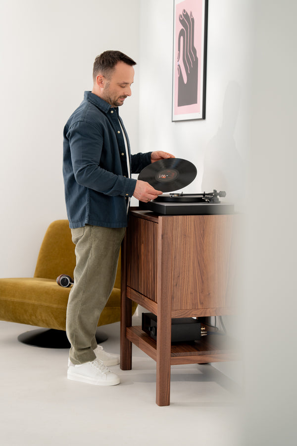 Man placing a vinyl record on a turntable in a stylish room with a yellow chair and modern art.