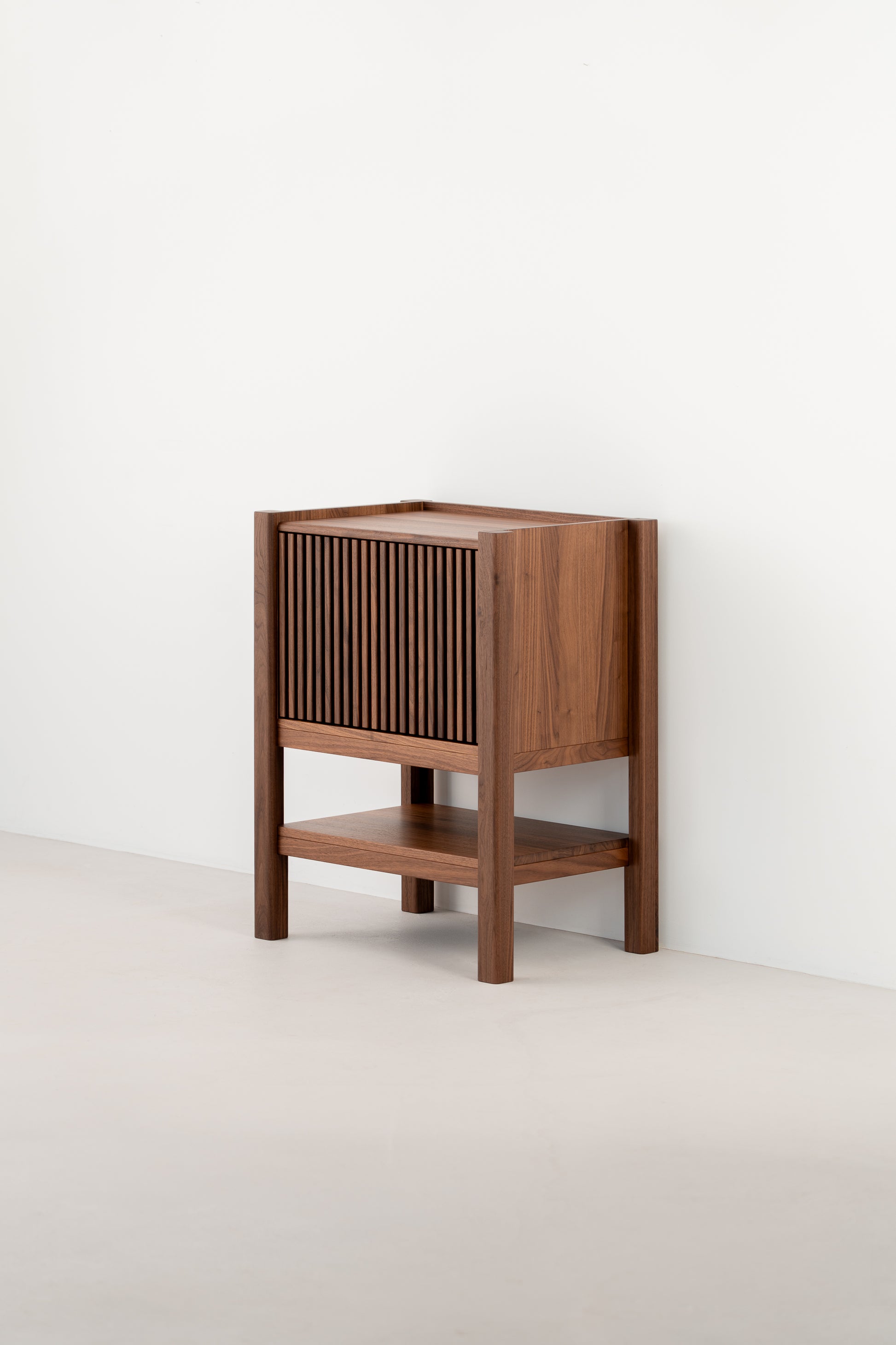  Wooden cabinet with slatted front, side view against a white wall.