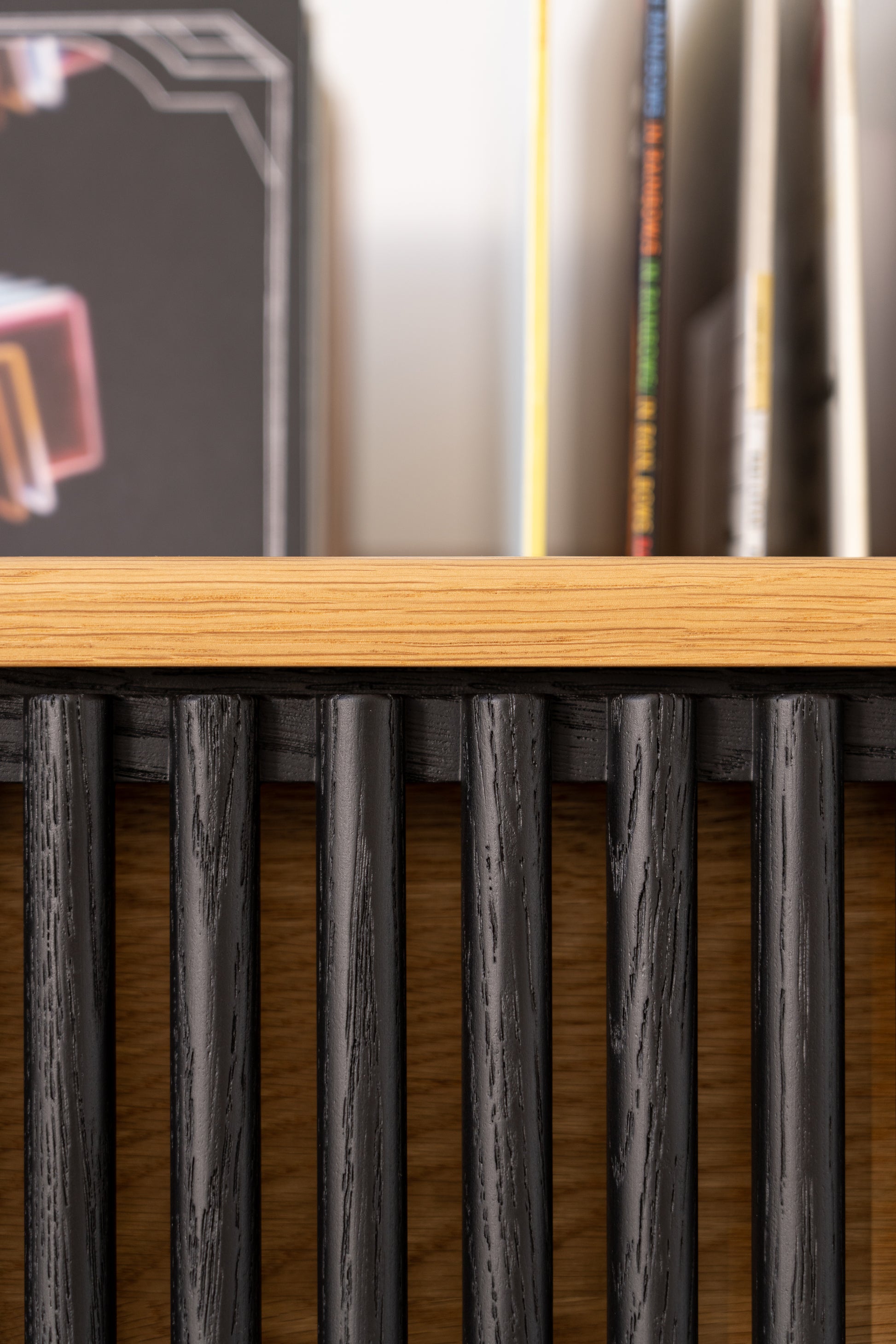 Close-up of a wooden shelf with vertical black slats, books visible in the background.