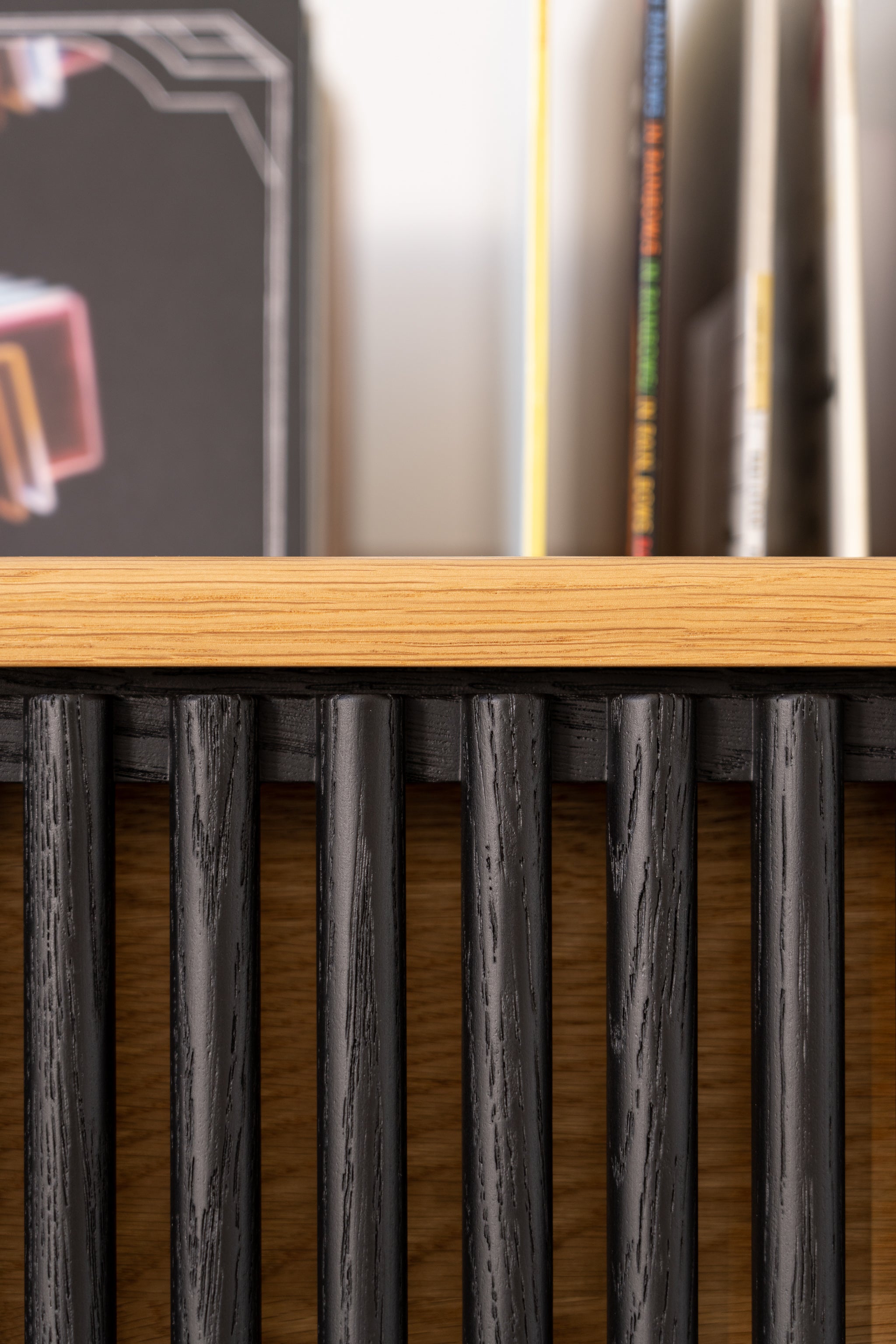 Close-up of a wooden shelf with vertical black slats, books visible in the background.