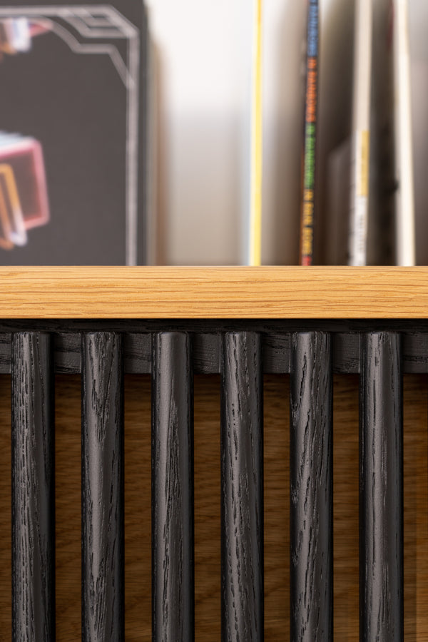Close-up of a wooden shelf with vertical black slats, books visible in the background.