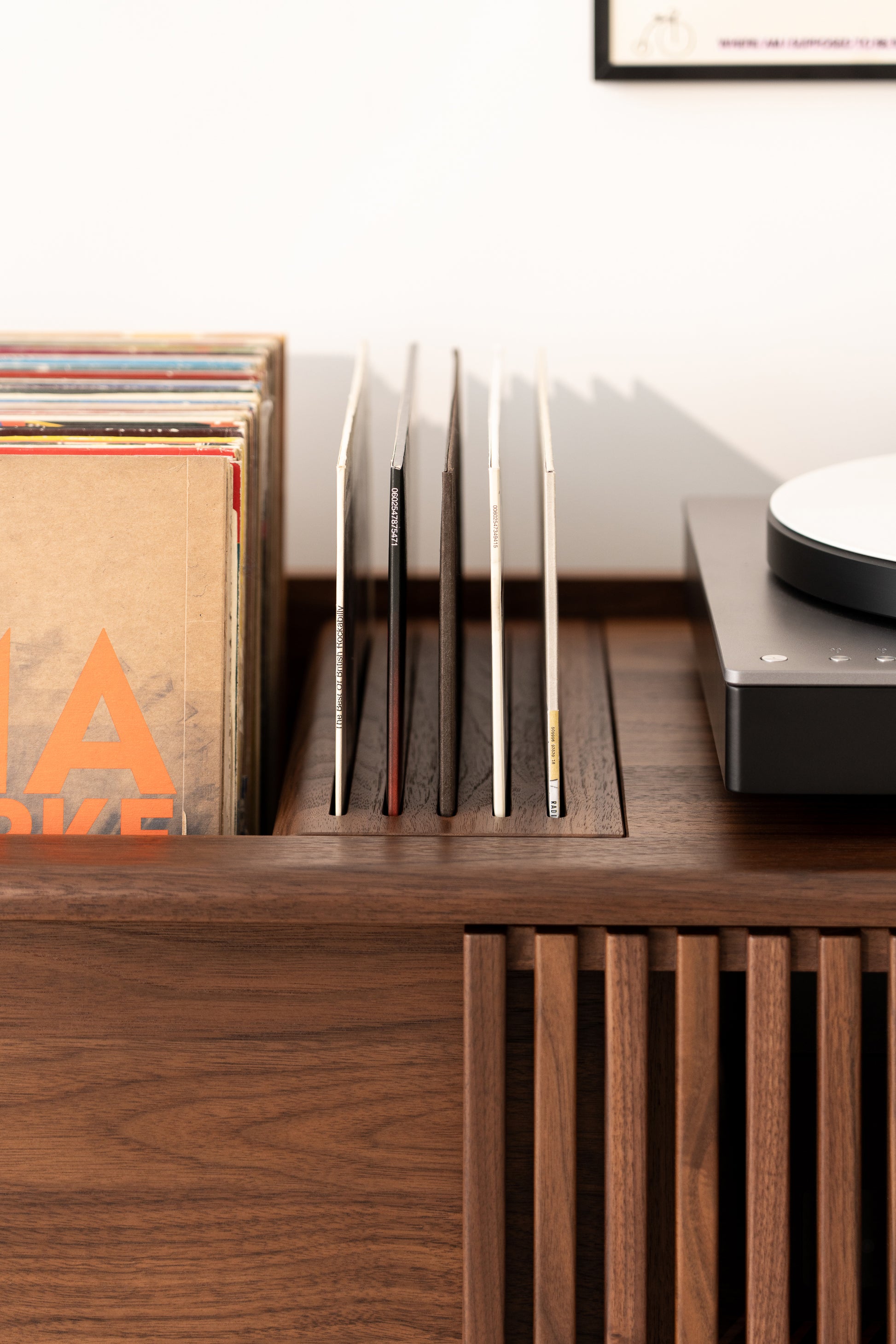 Vinyl records on a wooden shelf next to a turntable.
