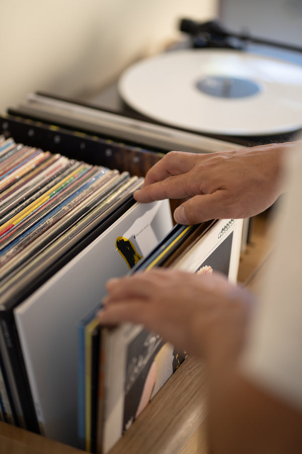 Hands browsing vinyl records next to a spinning white record on a turntable.