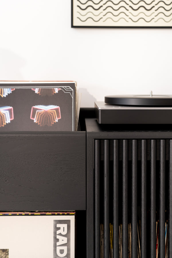 Vinyl records next to a turntable with a framed wavy line artwork on the wall.