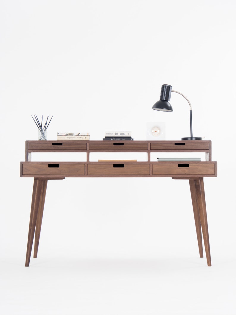 Wooden desk with five drawers, books, a table lamp, and a reed diffuser on top.