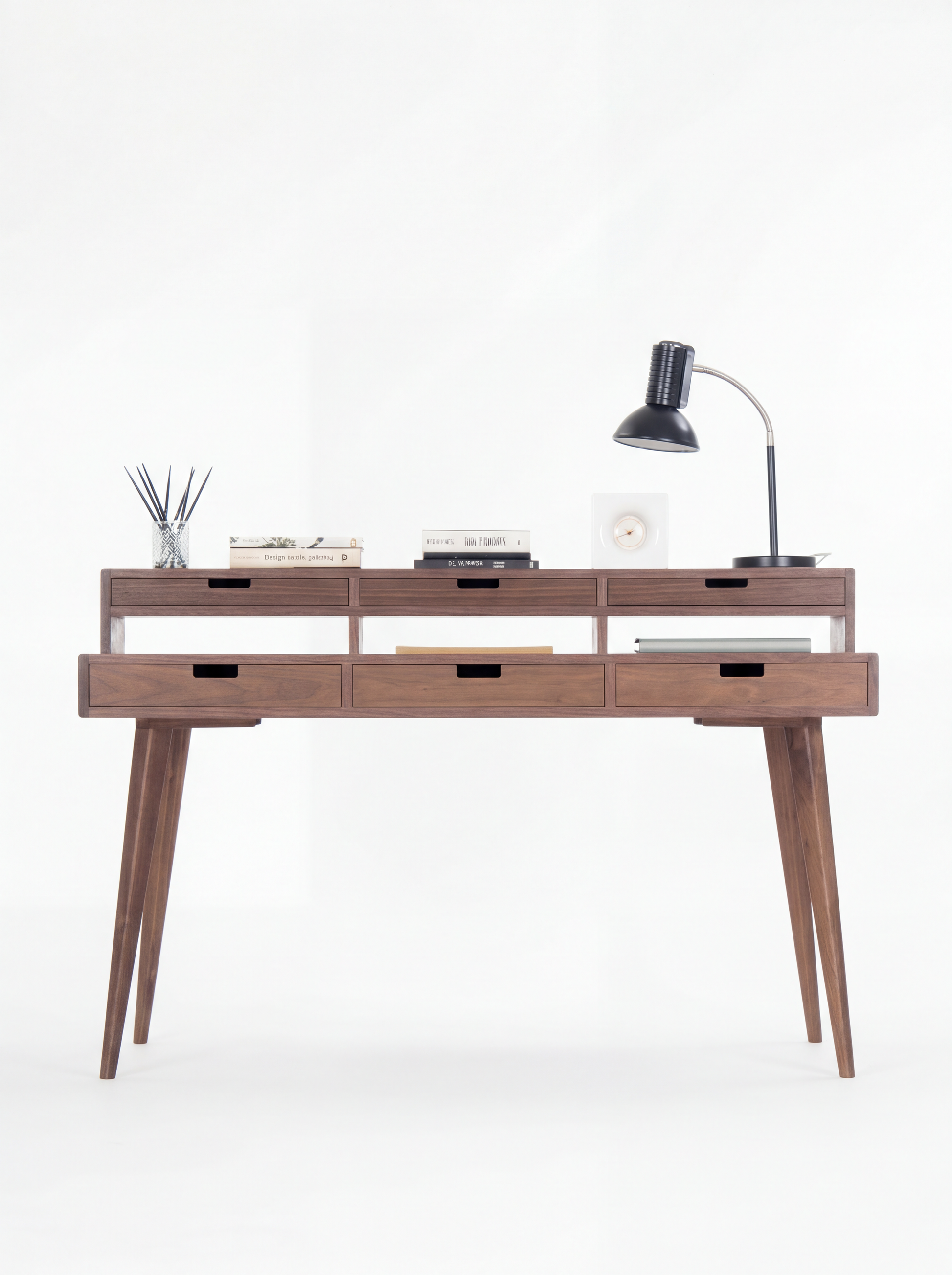 Wooden desk with five drawers, books, a table lamp, and a reed diffuser on top.