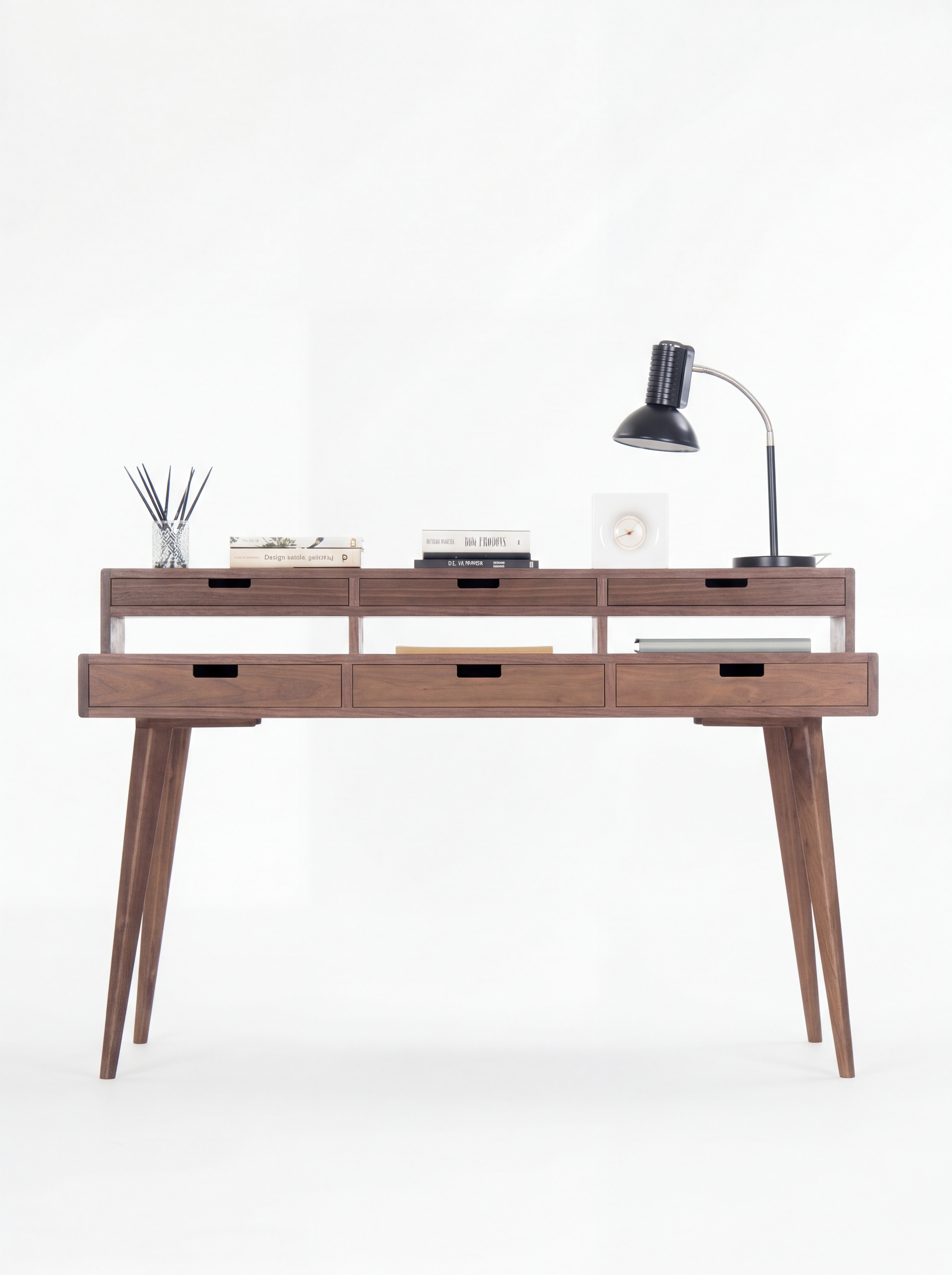Wooden desk with five drawers, books, a table lamp, and a reed diffuser on top.
