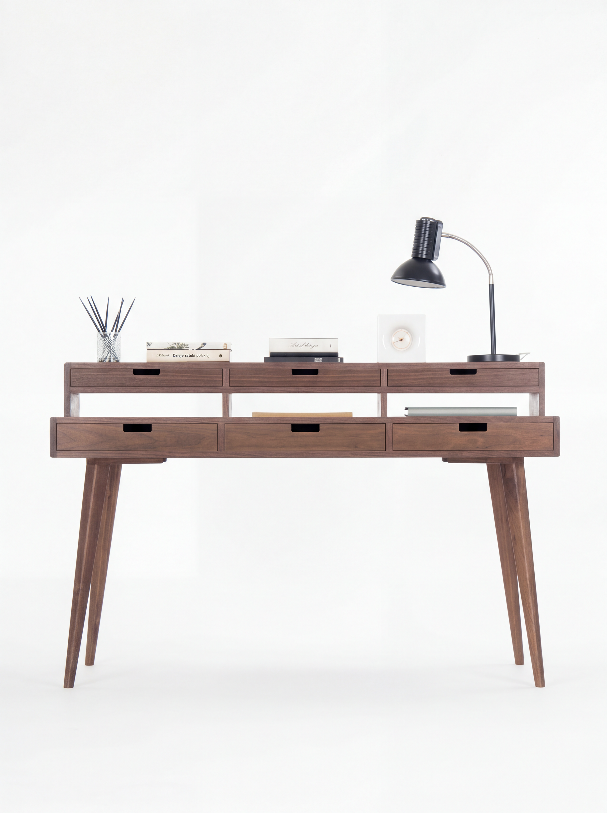 Wooden desk with five drawers, books, a table lamp, and a reed diffuser on top.