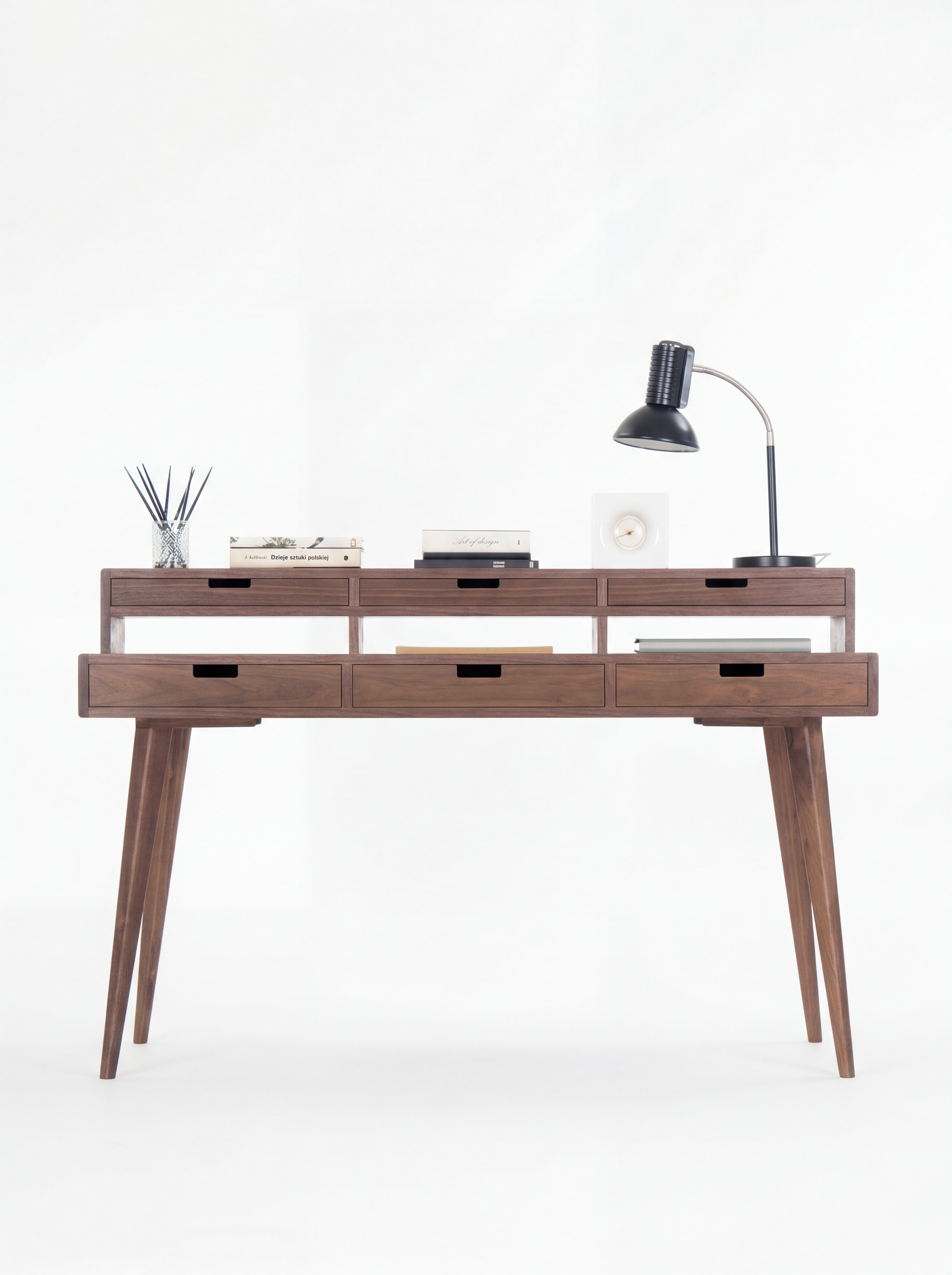 Wooden desk with five drawers, books, a table lamp, and a reed diffuser on top.