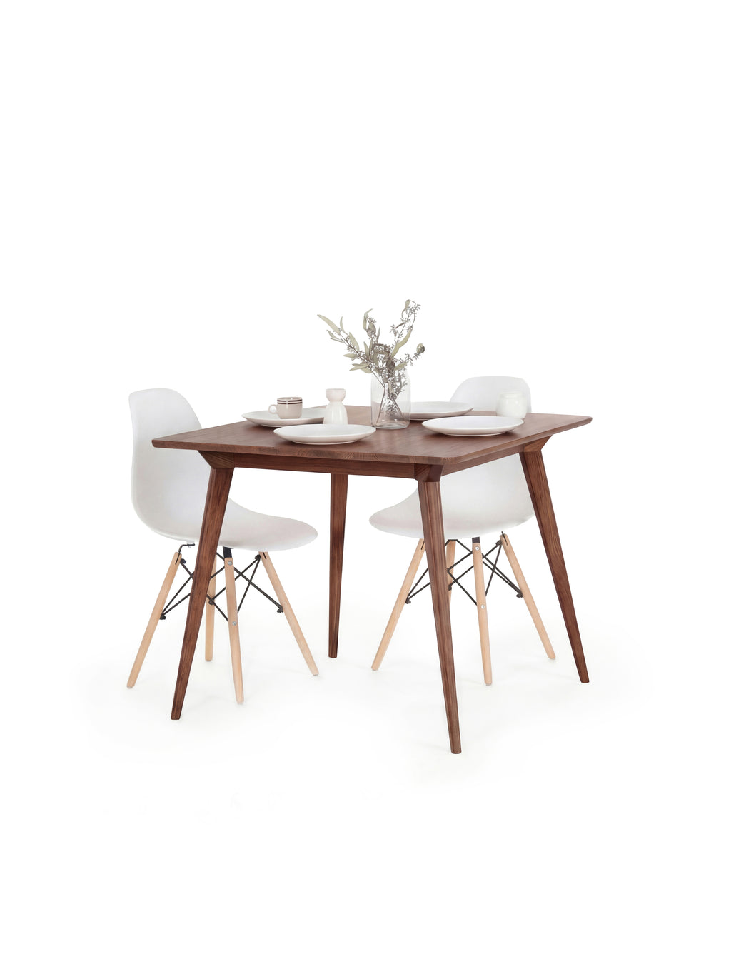 Wooden dining table with two white chairs, set for two with plates, cups, and a vase of flowers.