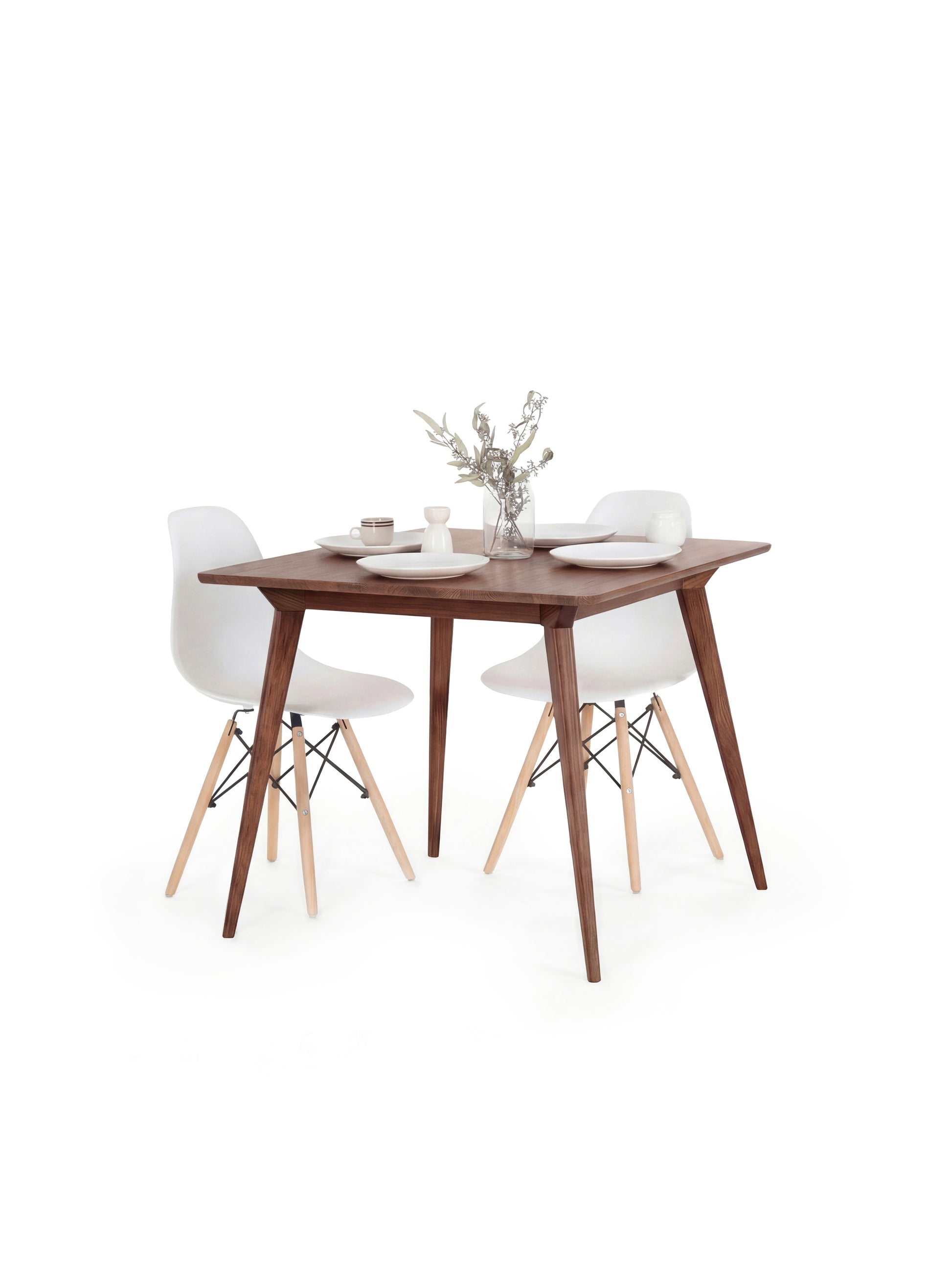 Wooden dining table with two white chairs, set for two with plates, cups, and a vase of flowers.