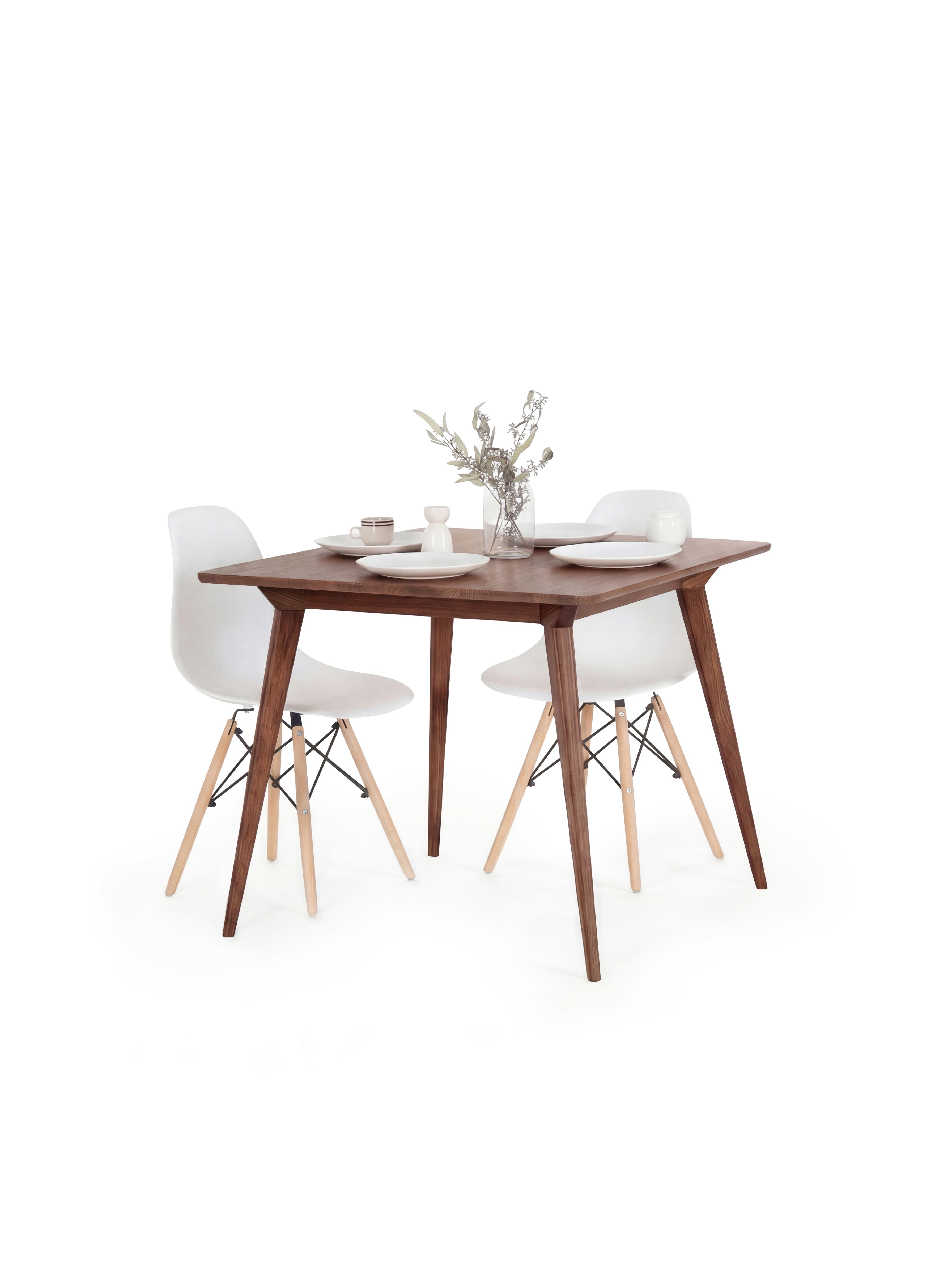 Wooden dining table with two white chairs, set for two with plates, cups, and a vase of flowers.