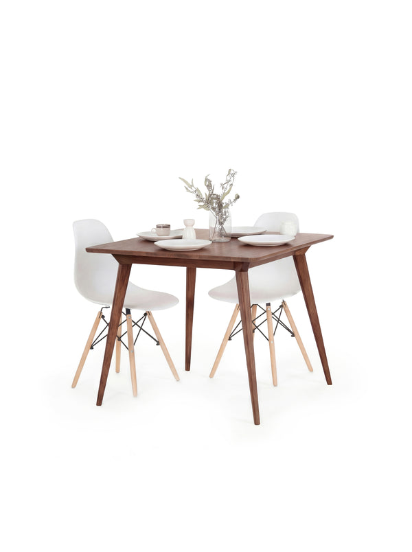 Wooden dining table with two white chairs, set for two with plates, cups, and a vase of flowers.