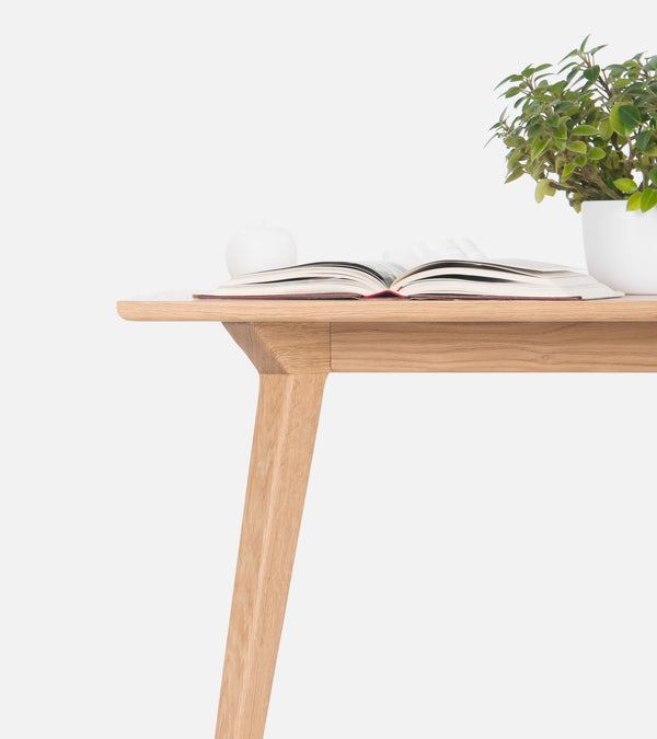 Wooden table with an open book, a white candle, and a potted plant on top.